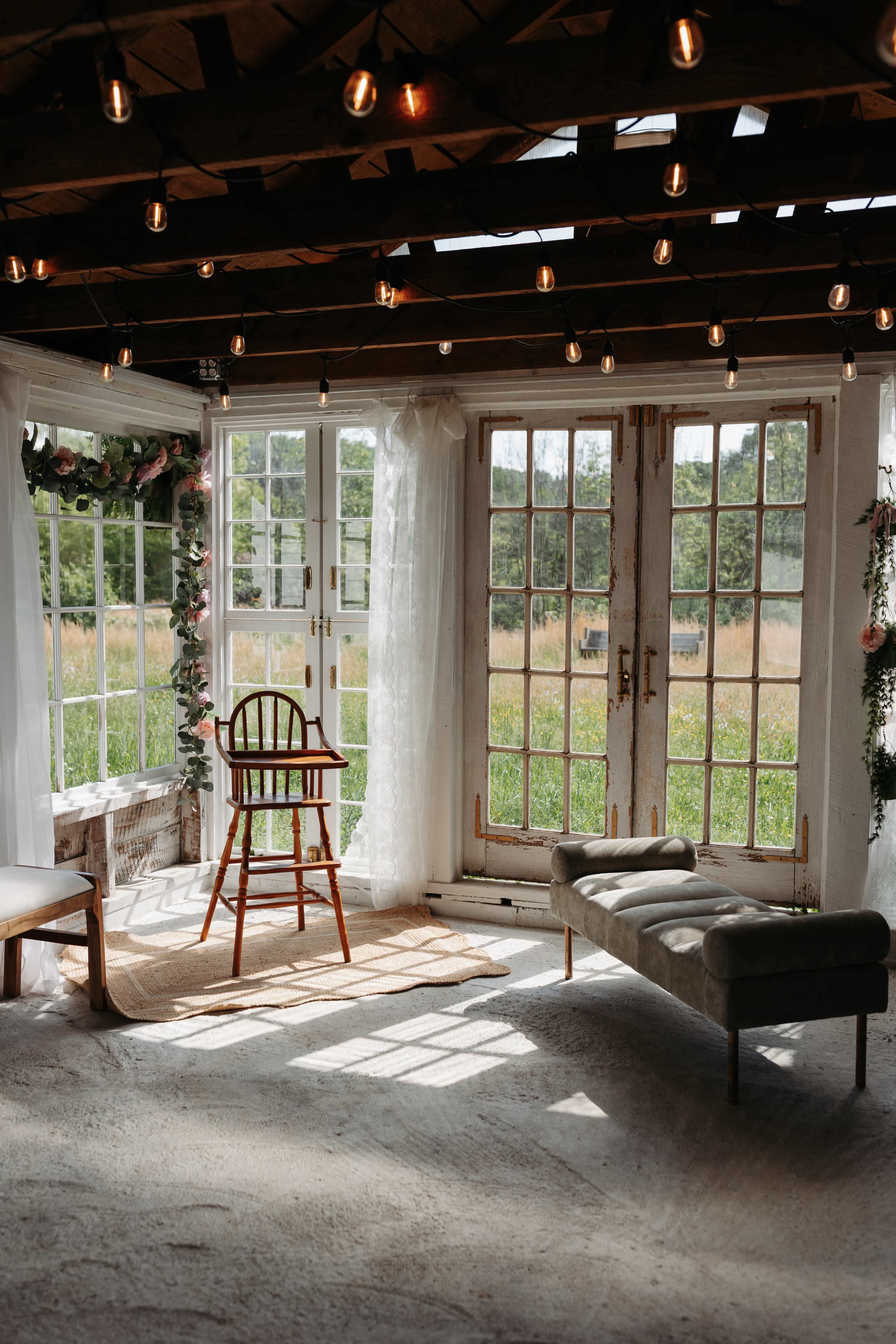 A bright room features large windows with a view of a grassy field, a wooden chair, and soft furnishings arranged around a light rug.