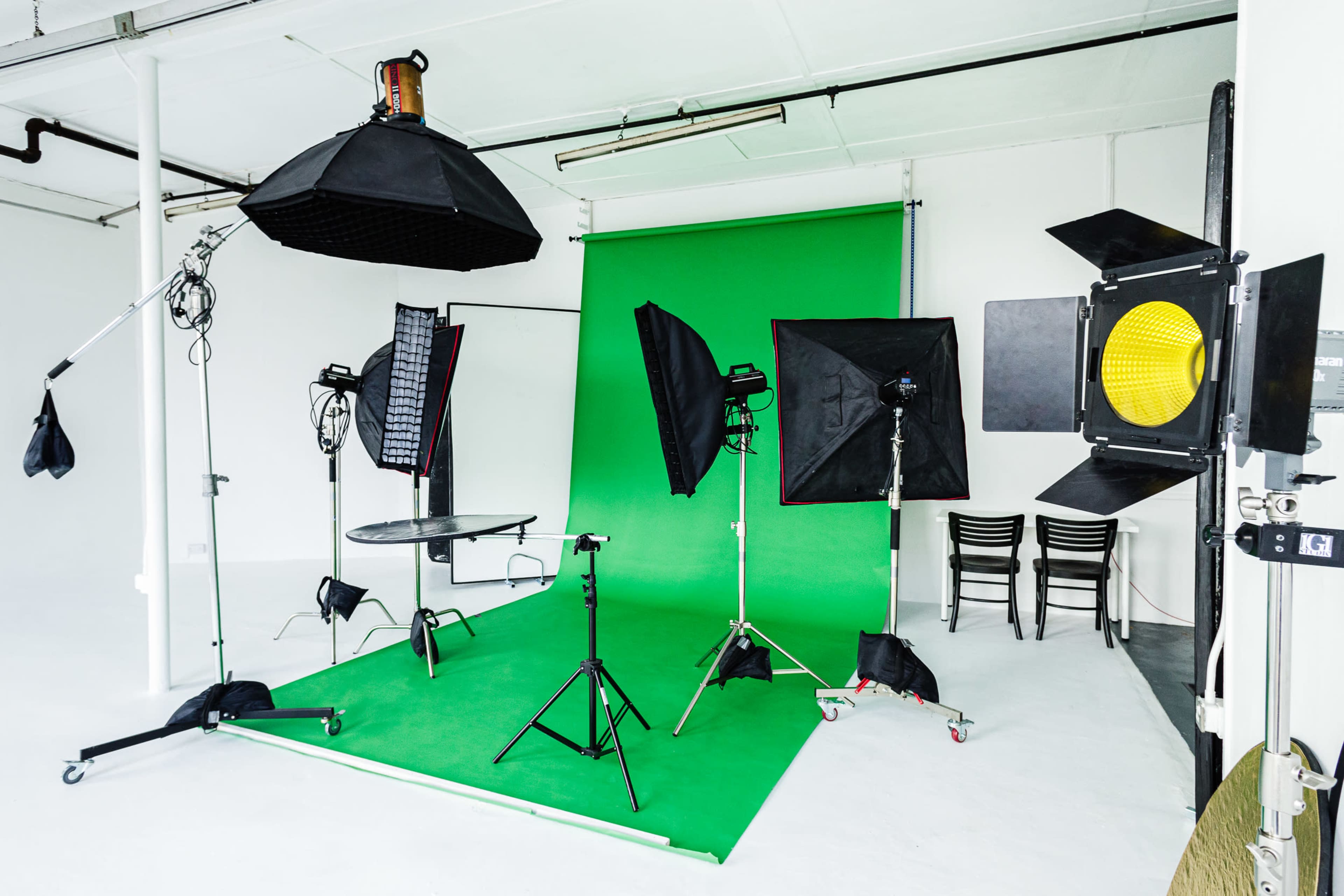 A photography studio is set up with a green backdrop, various lighting equipment, and a circular table in the center.