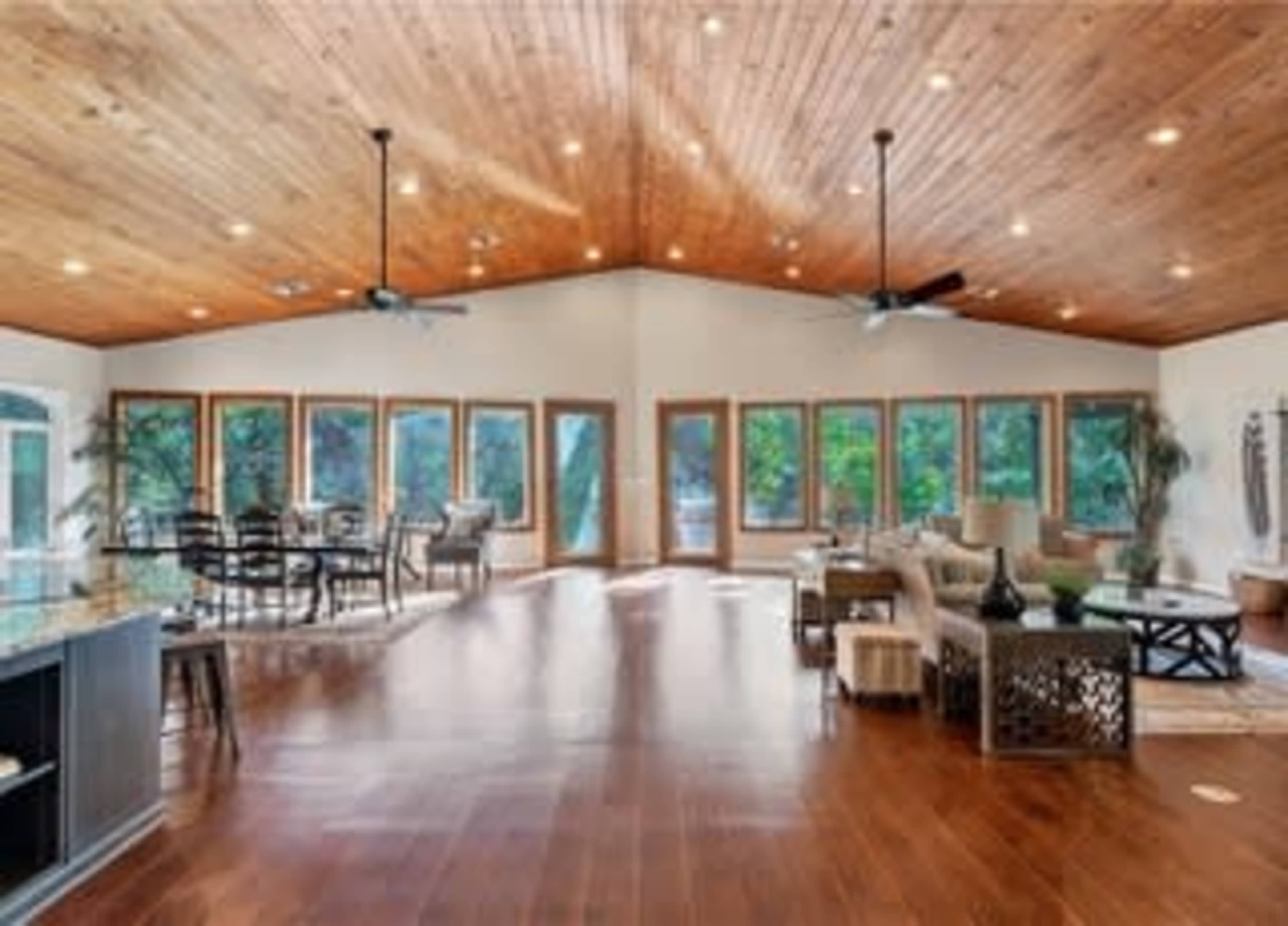 A spacious room features a high wooden ceiling, large windows, and various seating arrangements.