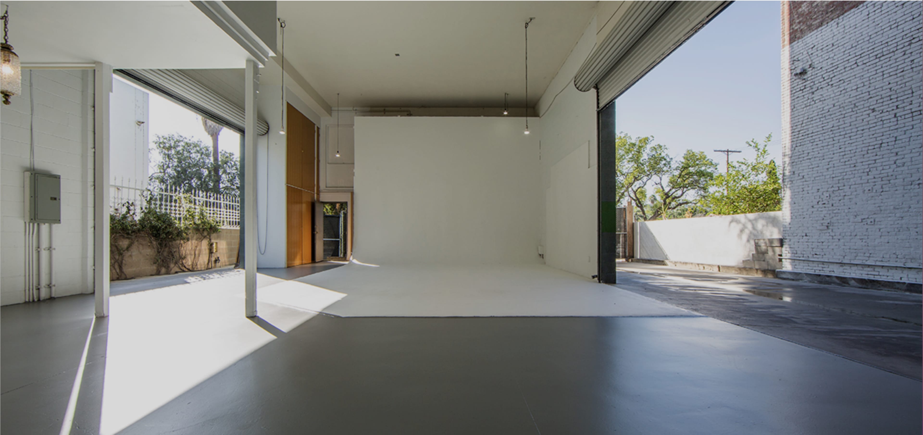 A modern, empty studio space with white walls and large windows that open to an outdoor area.