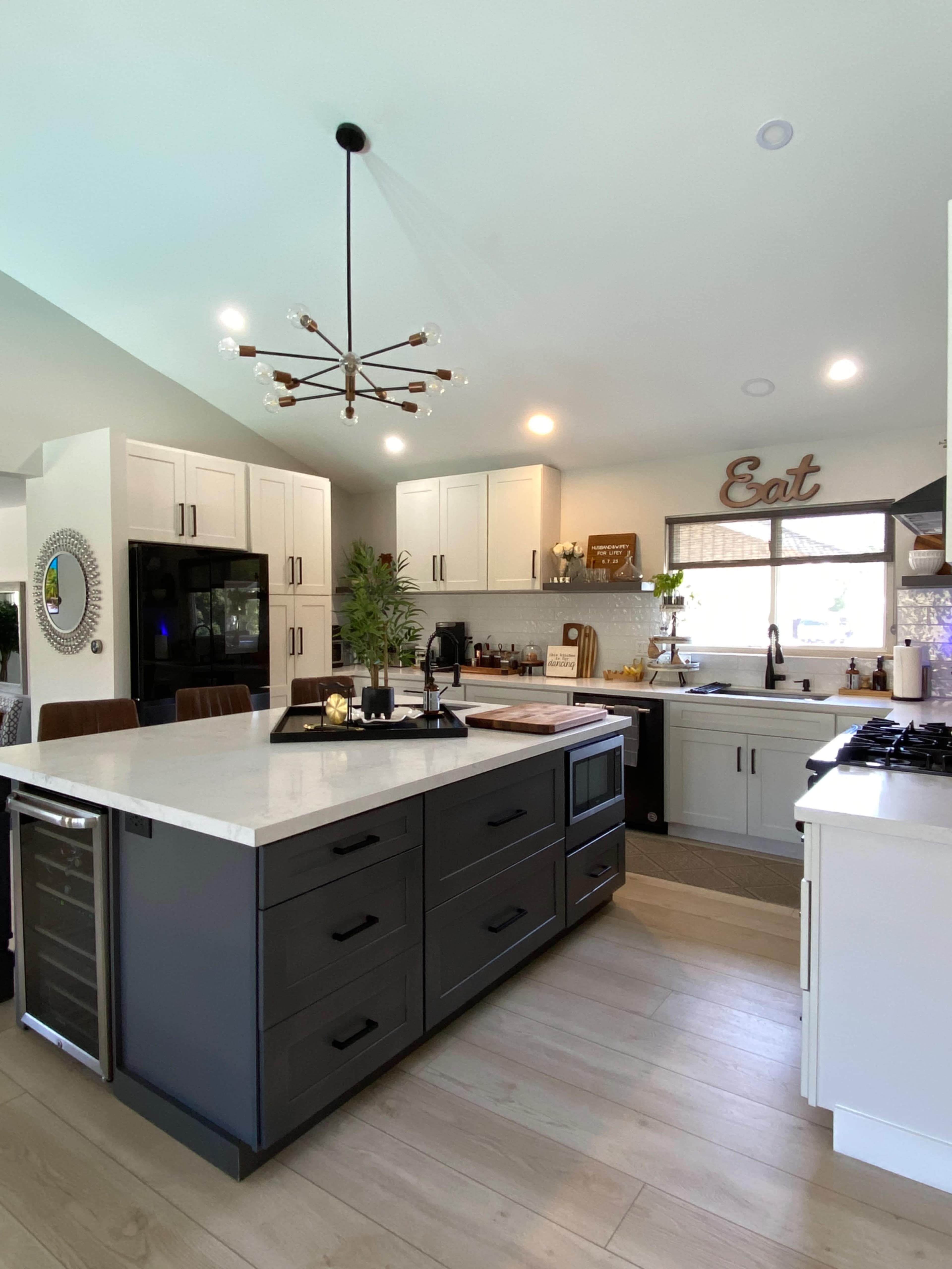 A modern kitchen features a central island with dark cabinetry, white countertops, and stainless steel appliances, along with a mix of open shelving and closed cabinets.
