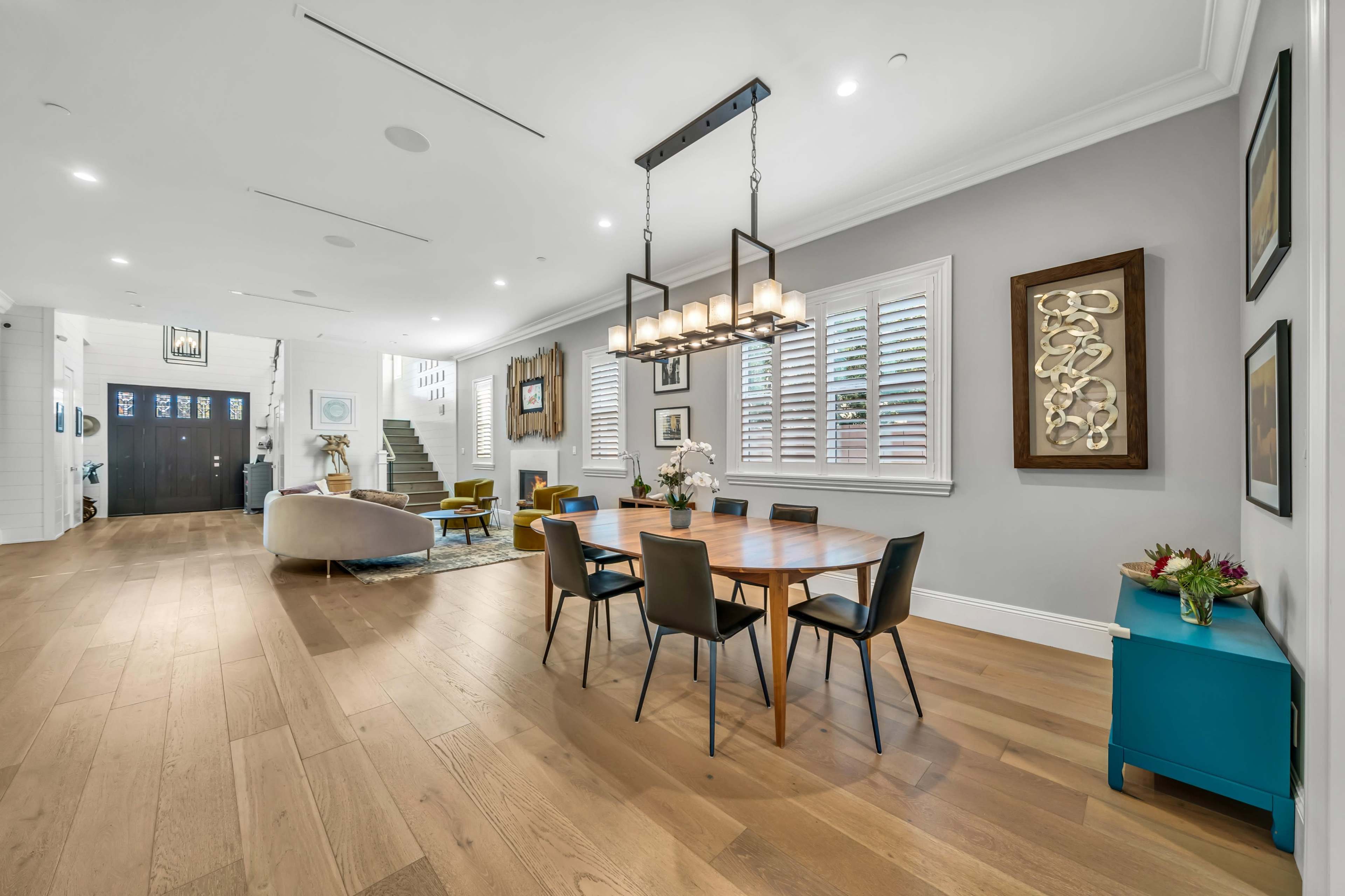 A modern dining area with a wooden table and eight chairs, adjacent to a spacious living area and a staircase.