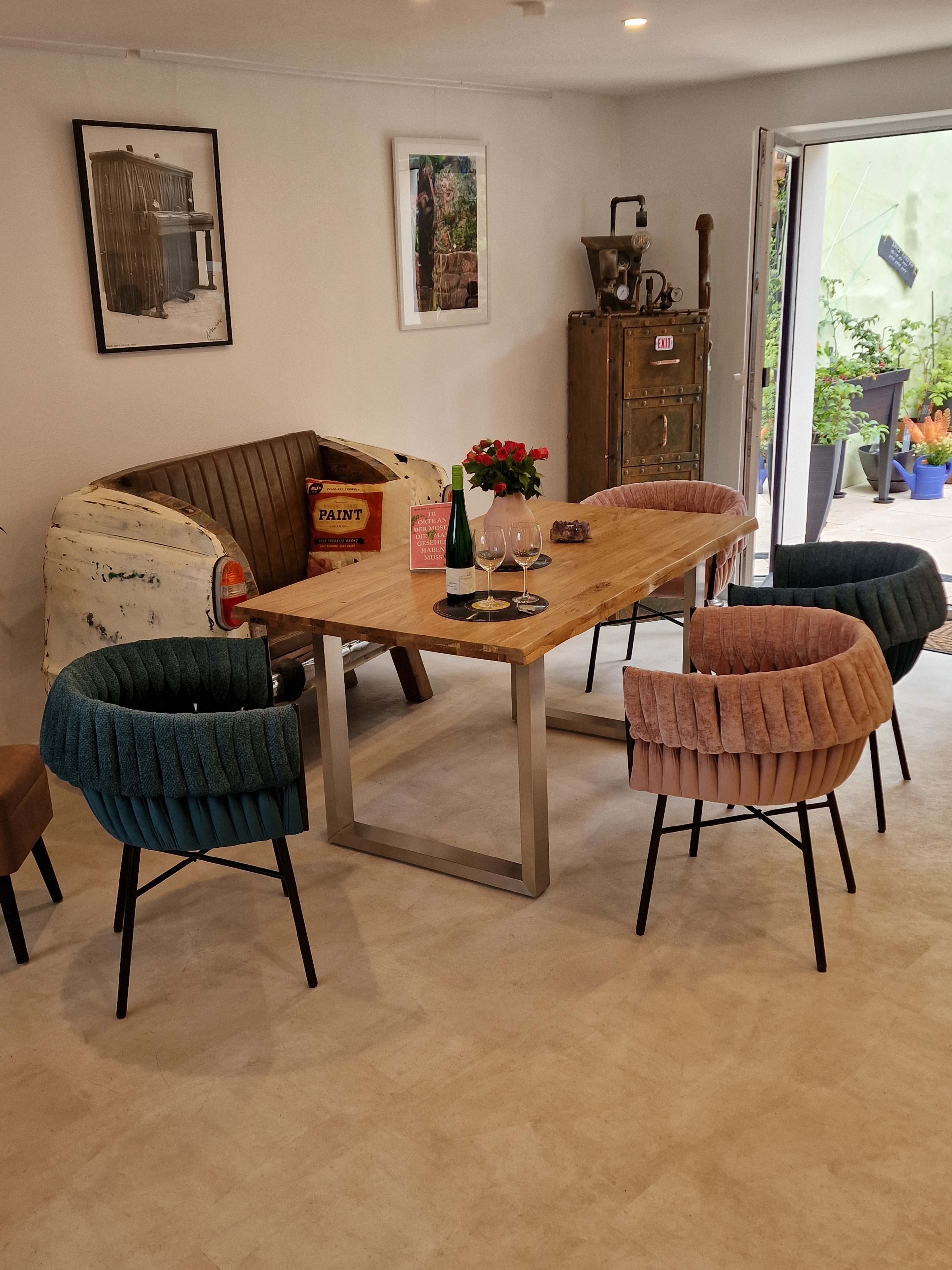 The image shows a cozy dining area featuring a wooden table surrounded by colorful upholstered chairs and a vintage sofa against a neutral wall.