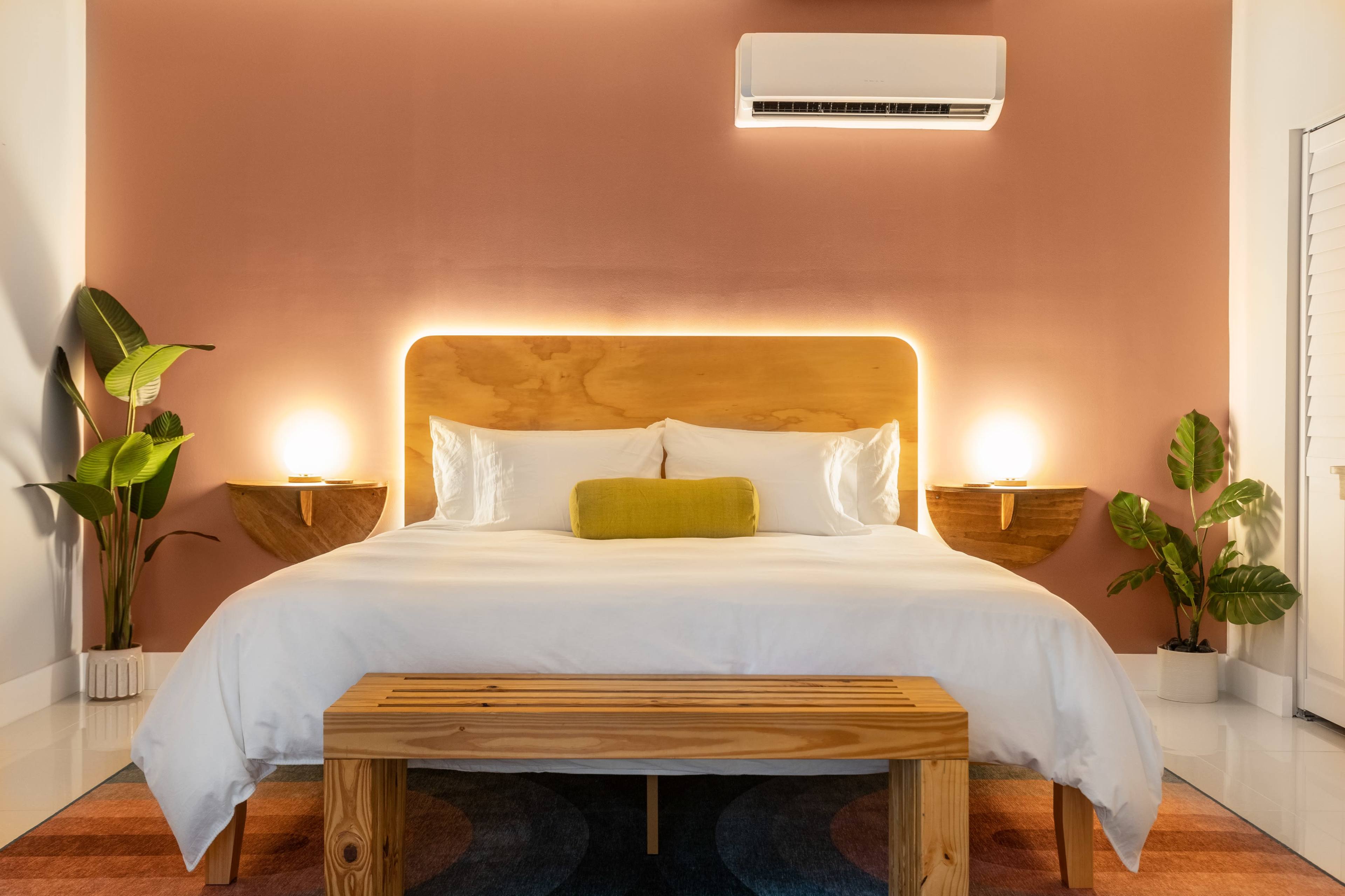 A modern bedroom features a wooden bed with a lighted headboard, accompanied by two bedside tables and decorative plants.