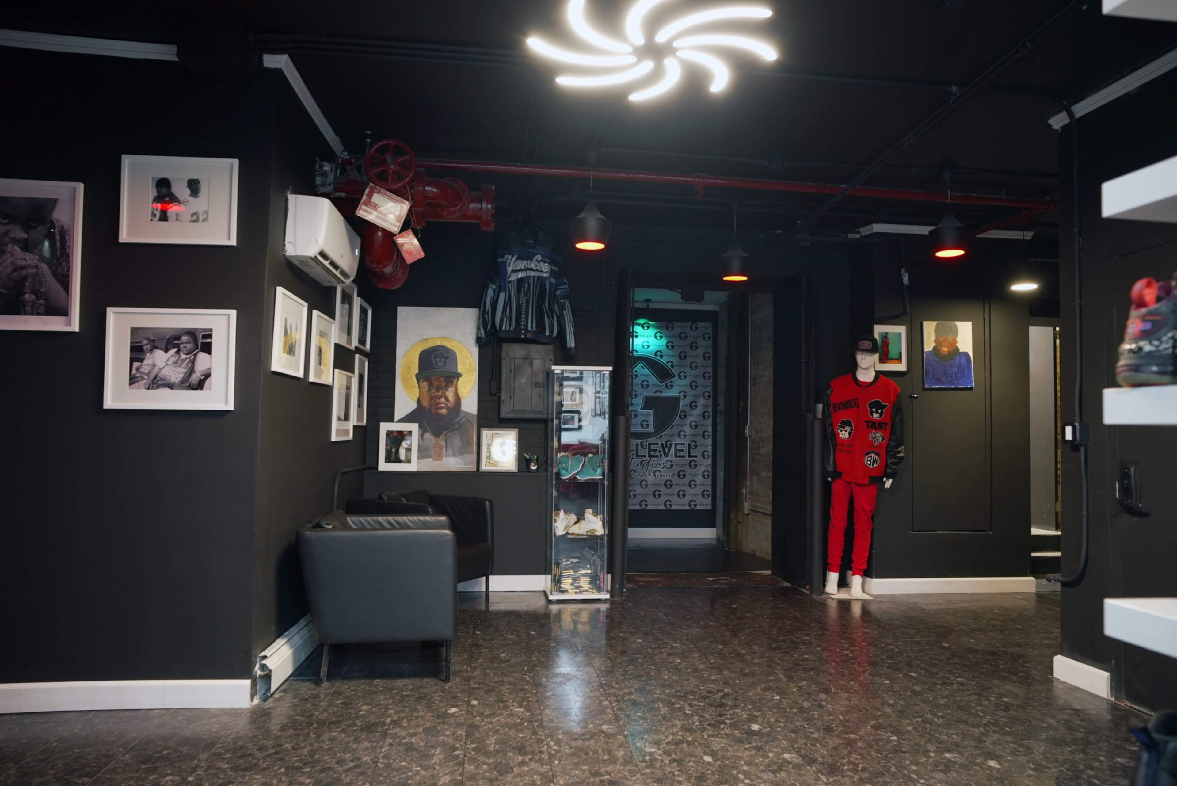 A modern interior space featuring black walls adorned with framed photographs and artwork, along with a mannequin dressed in red, and a seating area with a black chair.
