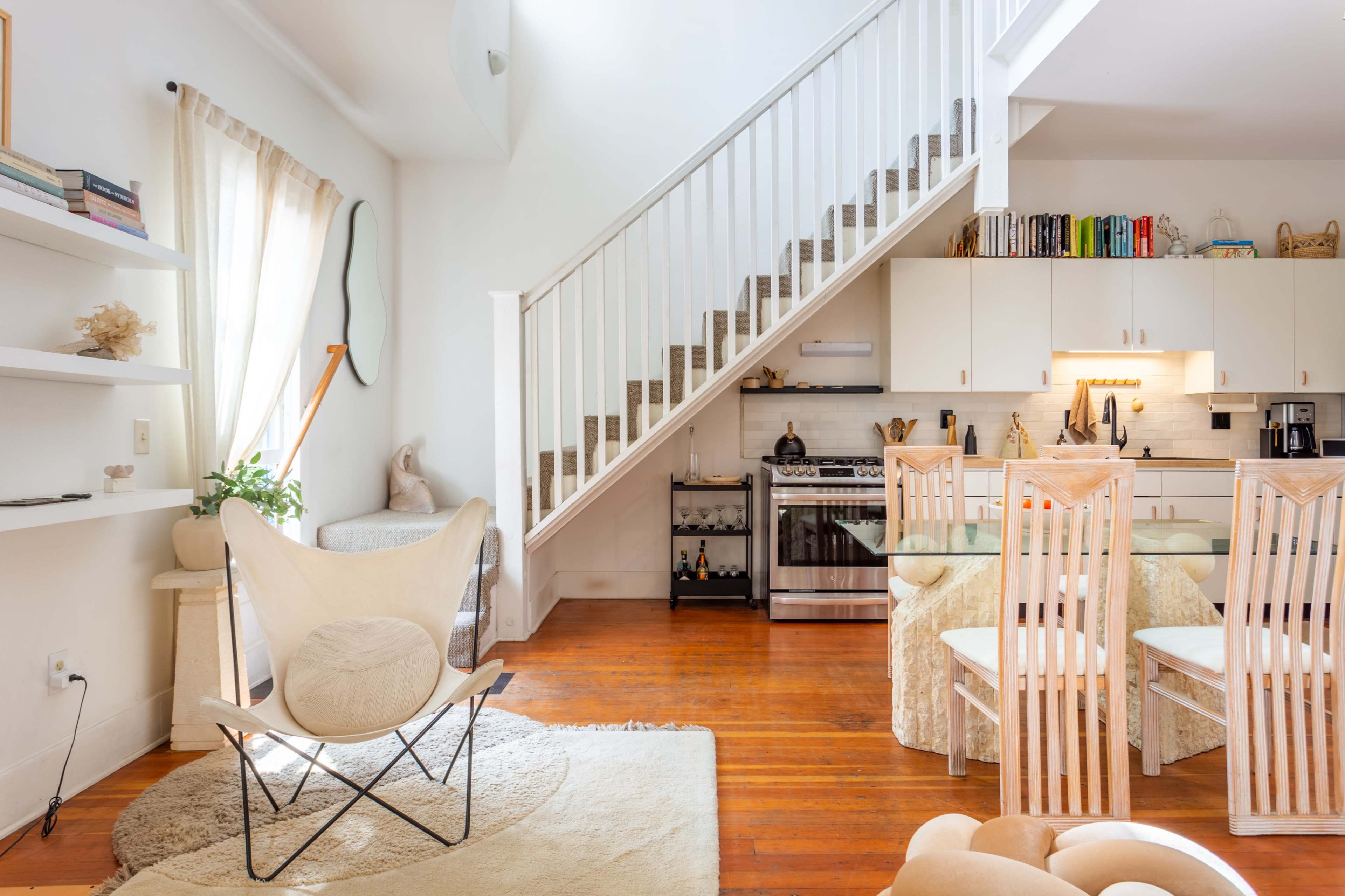 A bright, modern living space with a staircase, a dining area, and a kitchen featuring stainless steel appliances.