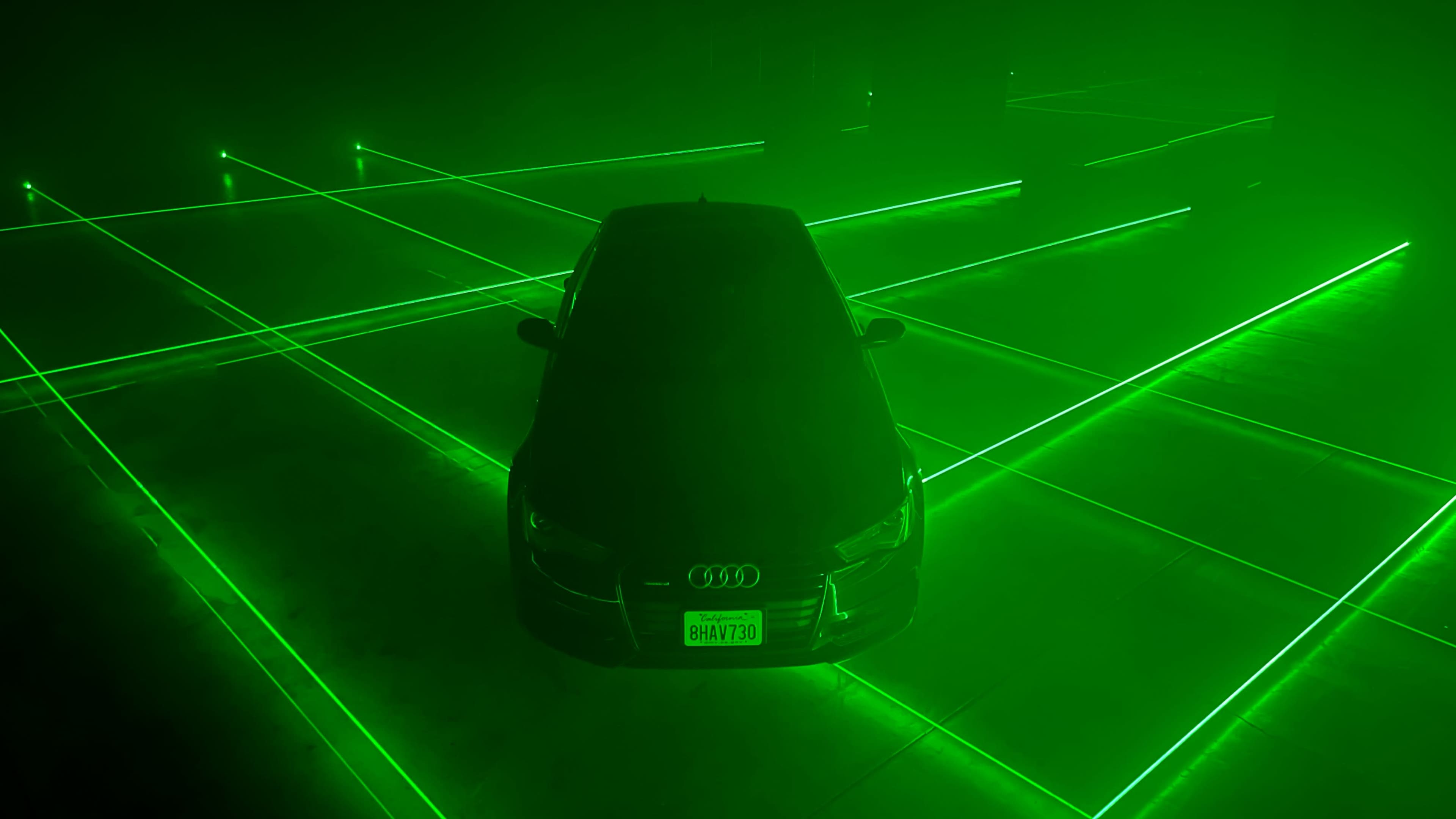 An Audi car is positioned centrally in a dimly lit space, surrounded by green laser grid lines.