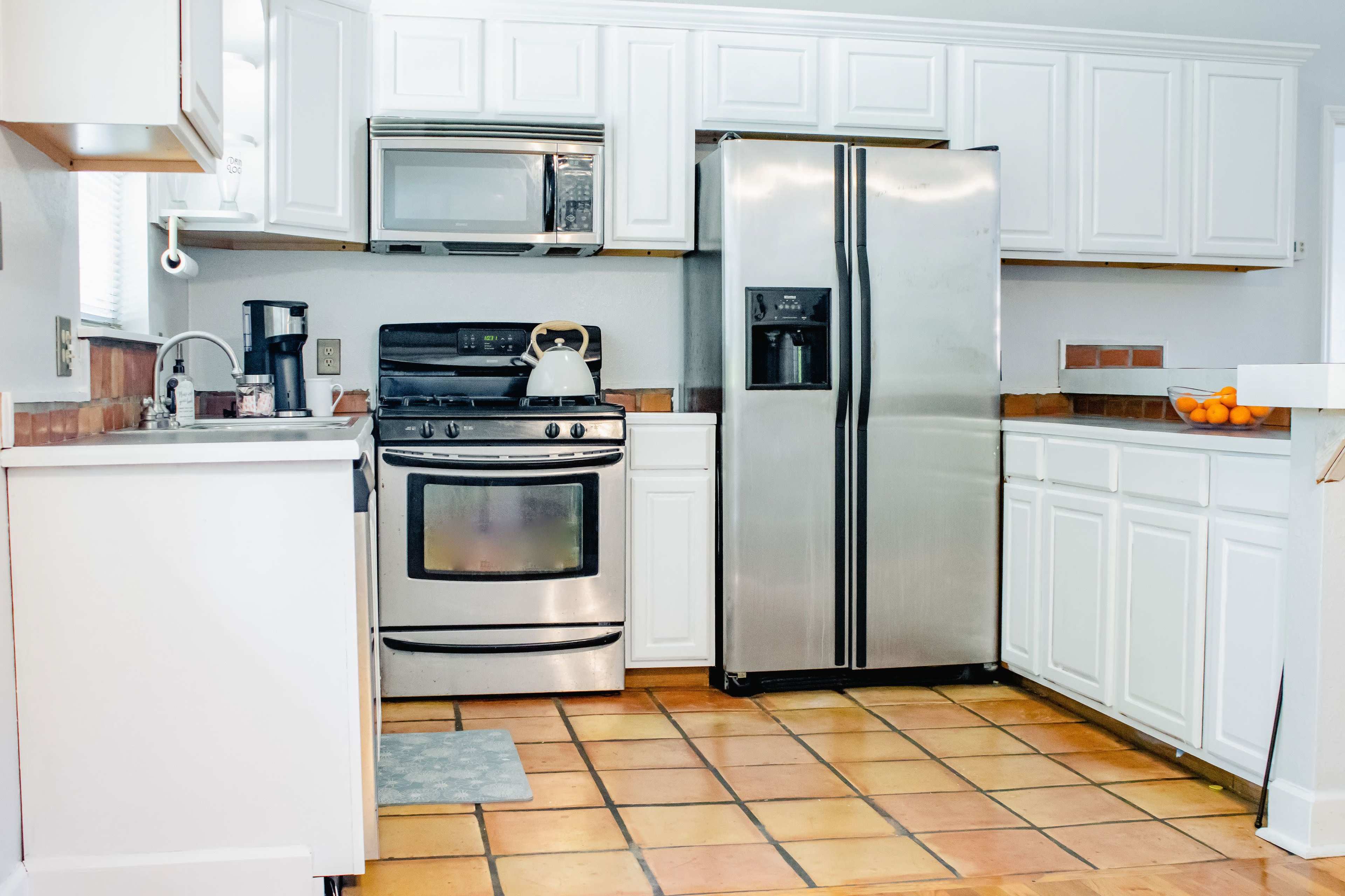 A kitchen with white cabinets, stainless steel appliances, and a tile floor.