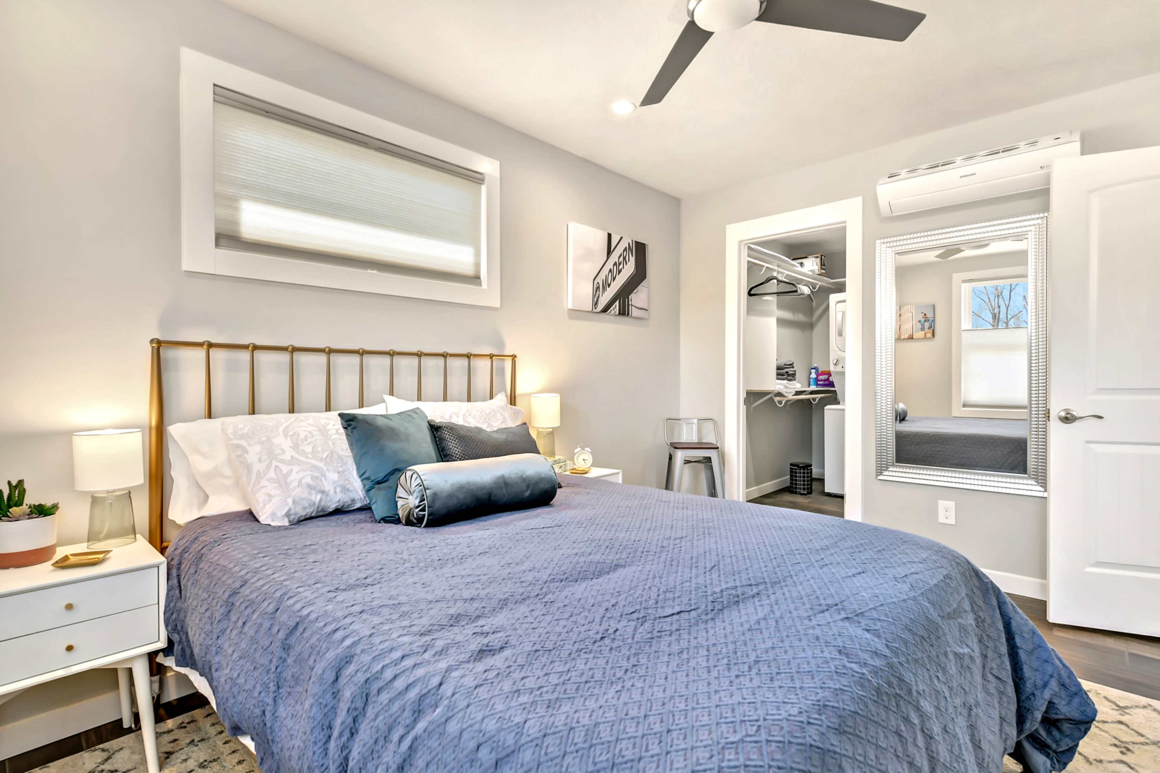 A neatly arranged bedroom features a bed with a blue comforter, a small nightstand with a lamp, and a closet visible through an open door.