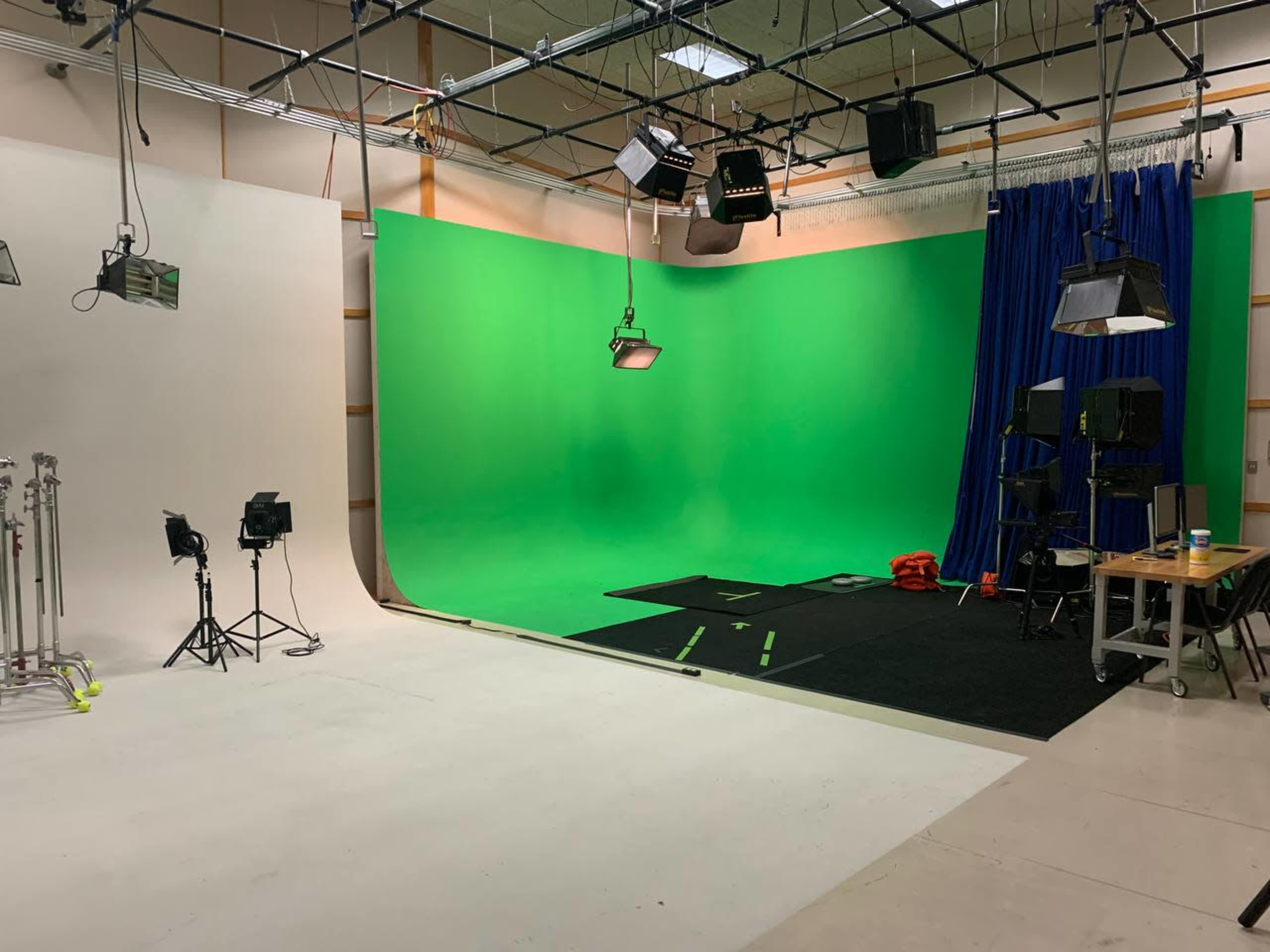 A spacious studio setup featuring a green screen, black carpet, various lighting equipment, and a table with additional items on one side.