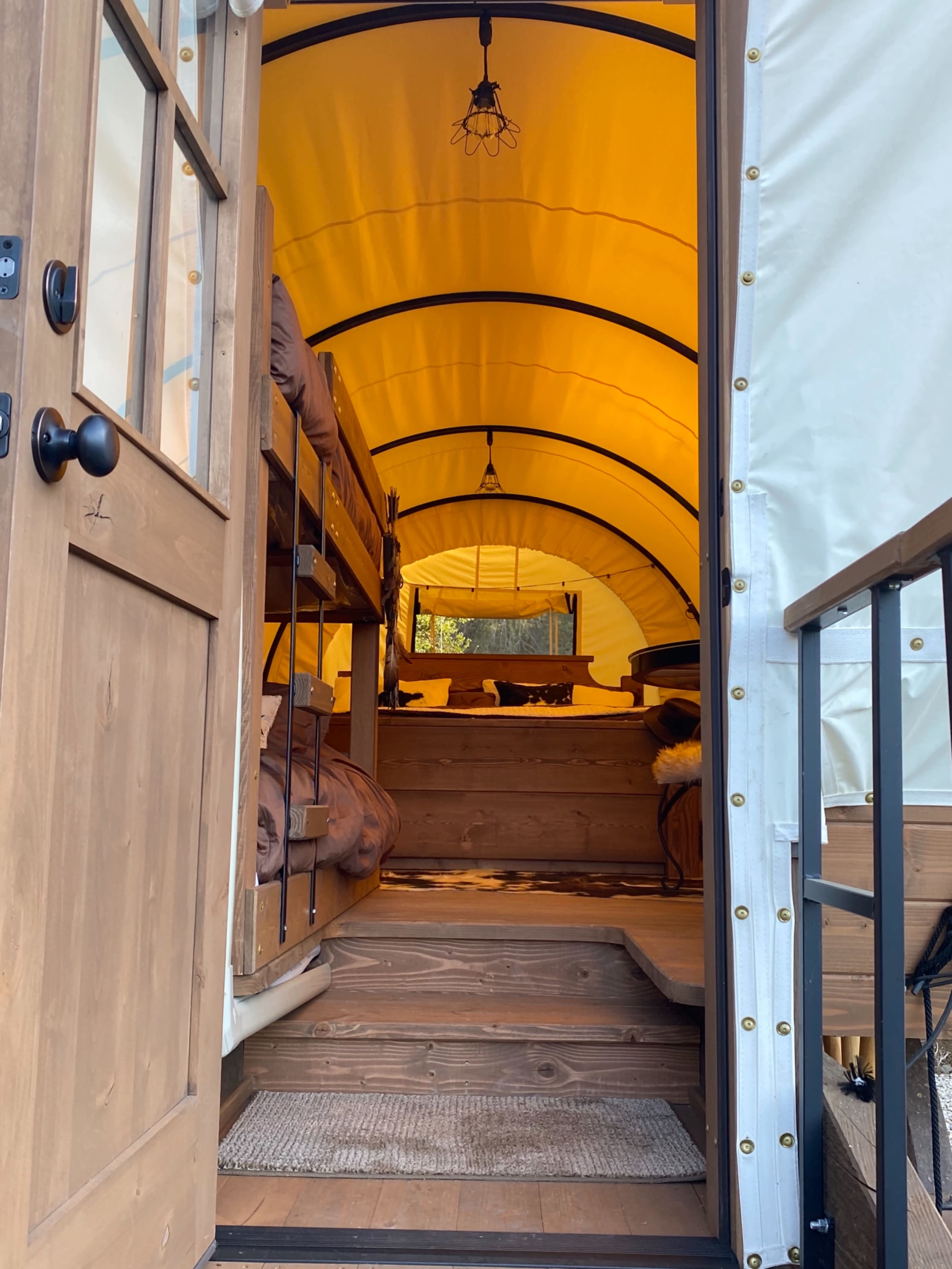 The interior of a canvas cabin, featuring a staircase leading to a double bunk bed on the left and a living area with a table and chairs at the far end.