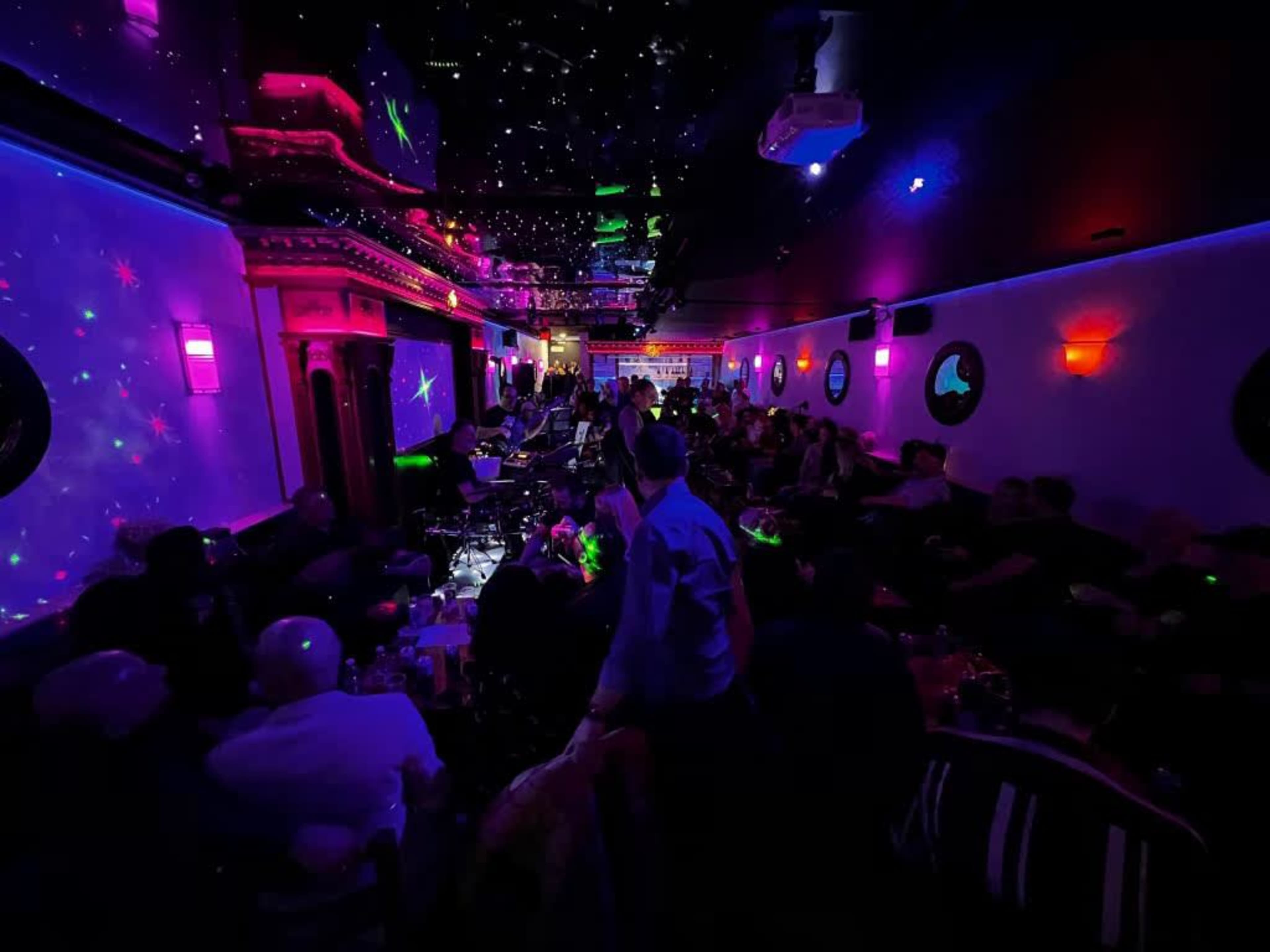 A crowded nightclub scene features colorful lighting and people enjoying live music in a vibrant atmosphere.