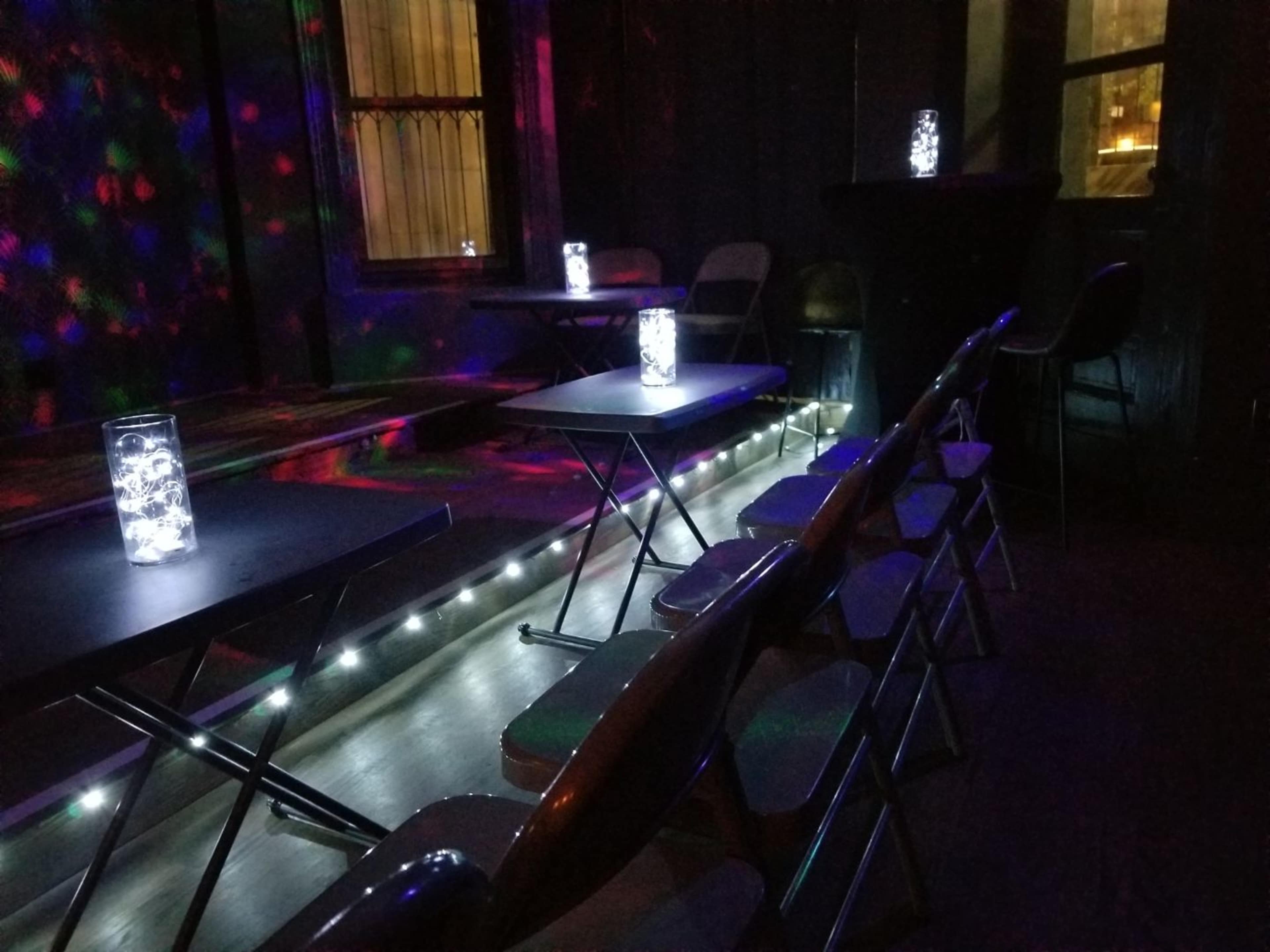 A dimly lit room with several folding chairs arranged in rows facing tables, each topped with illuminated glass containers.