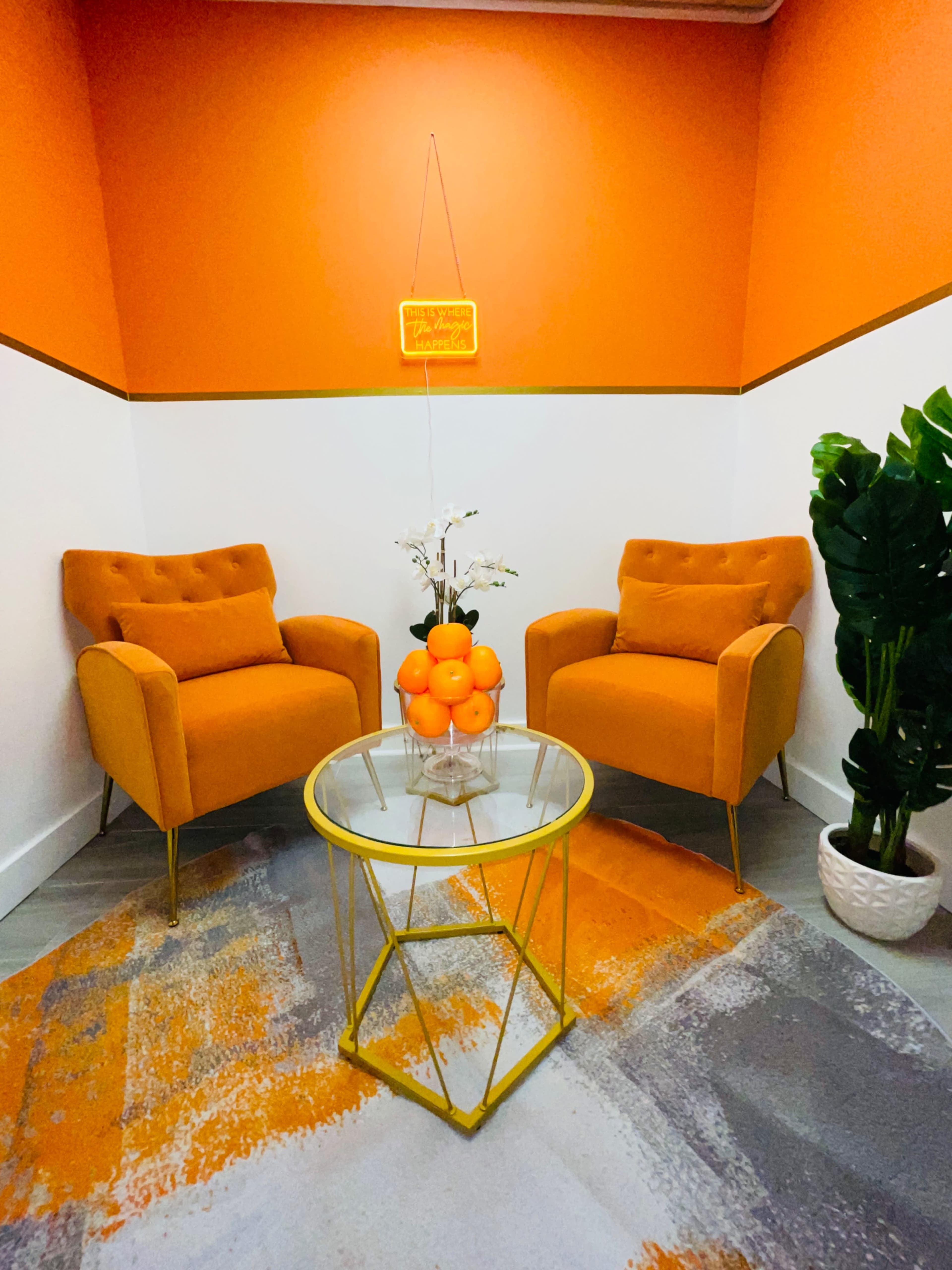 A bright orange room with two matching upholstered chairs, a glass table with a bowl of oranges, and a potted plant.