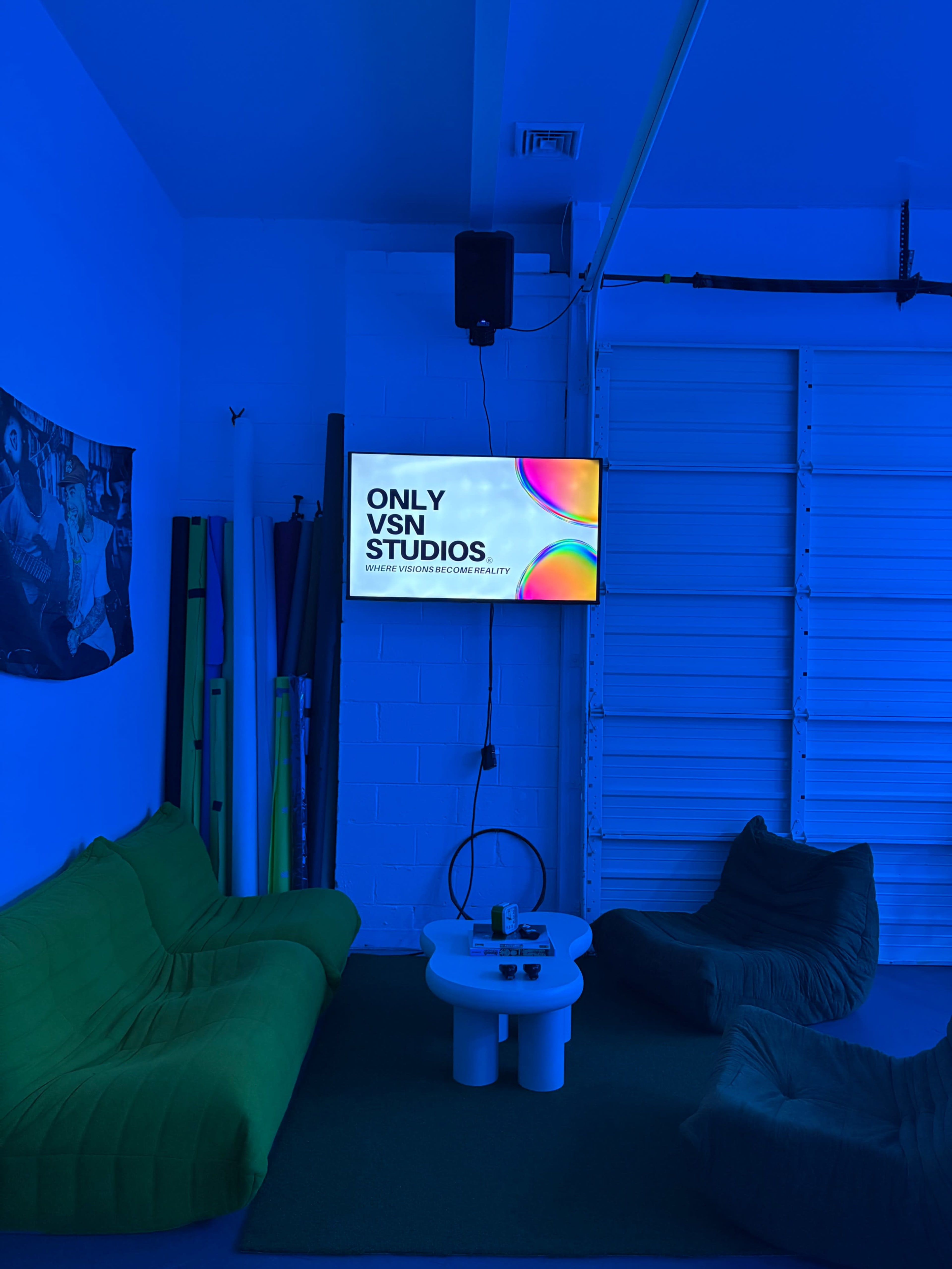 A blue-lit studio featuring a television displaying the text "ONLY VSN STUDIOS" along with a green couch, bean bags, and various colored props in the background.