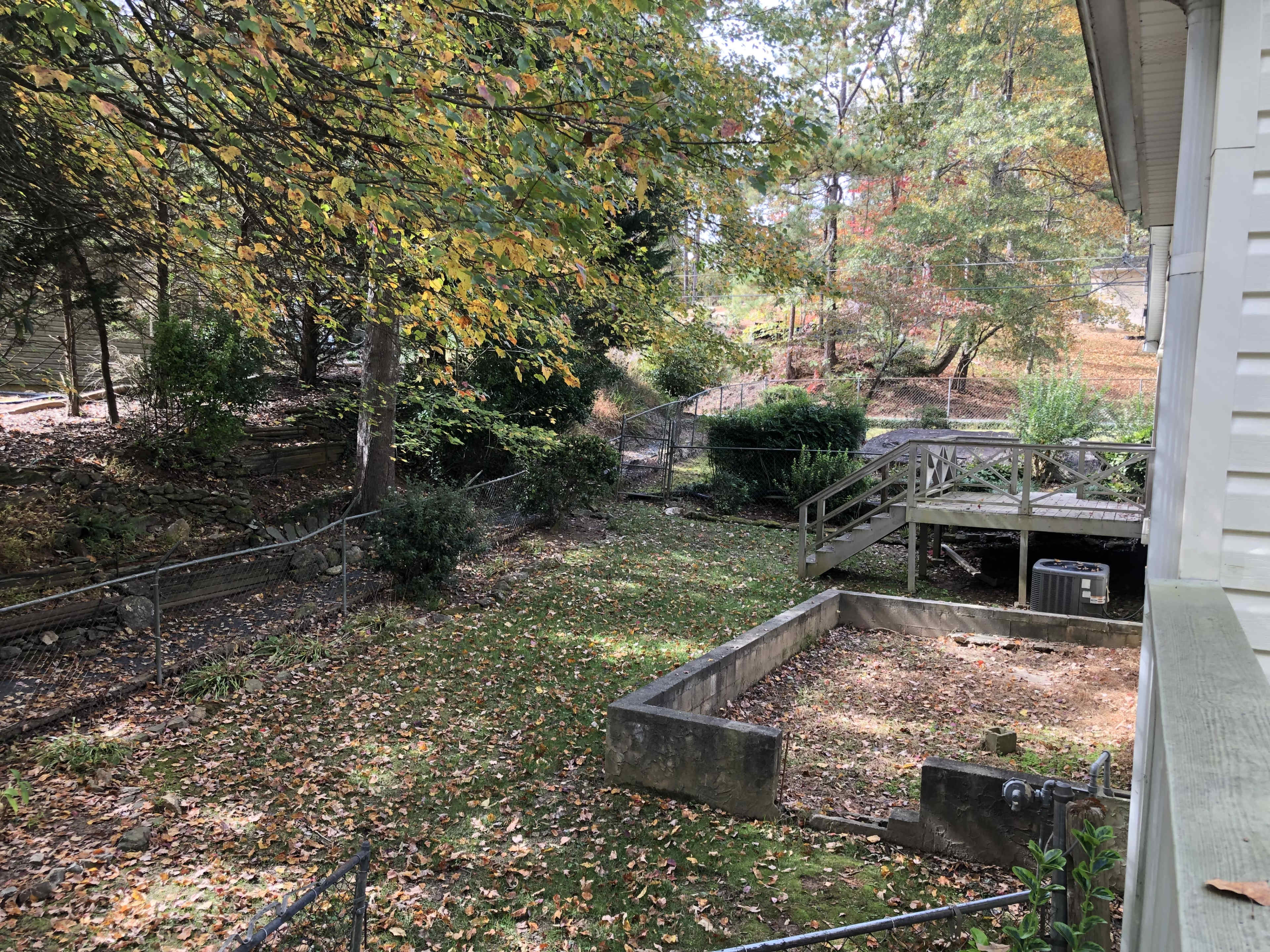 The image shows a fenced backyard with a wooden deck, surrounded by trees and scattered leaves on the ground.