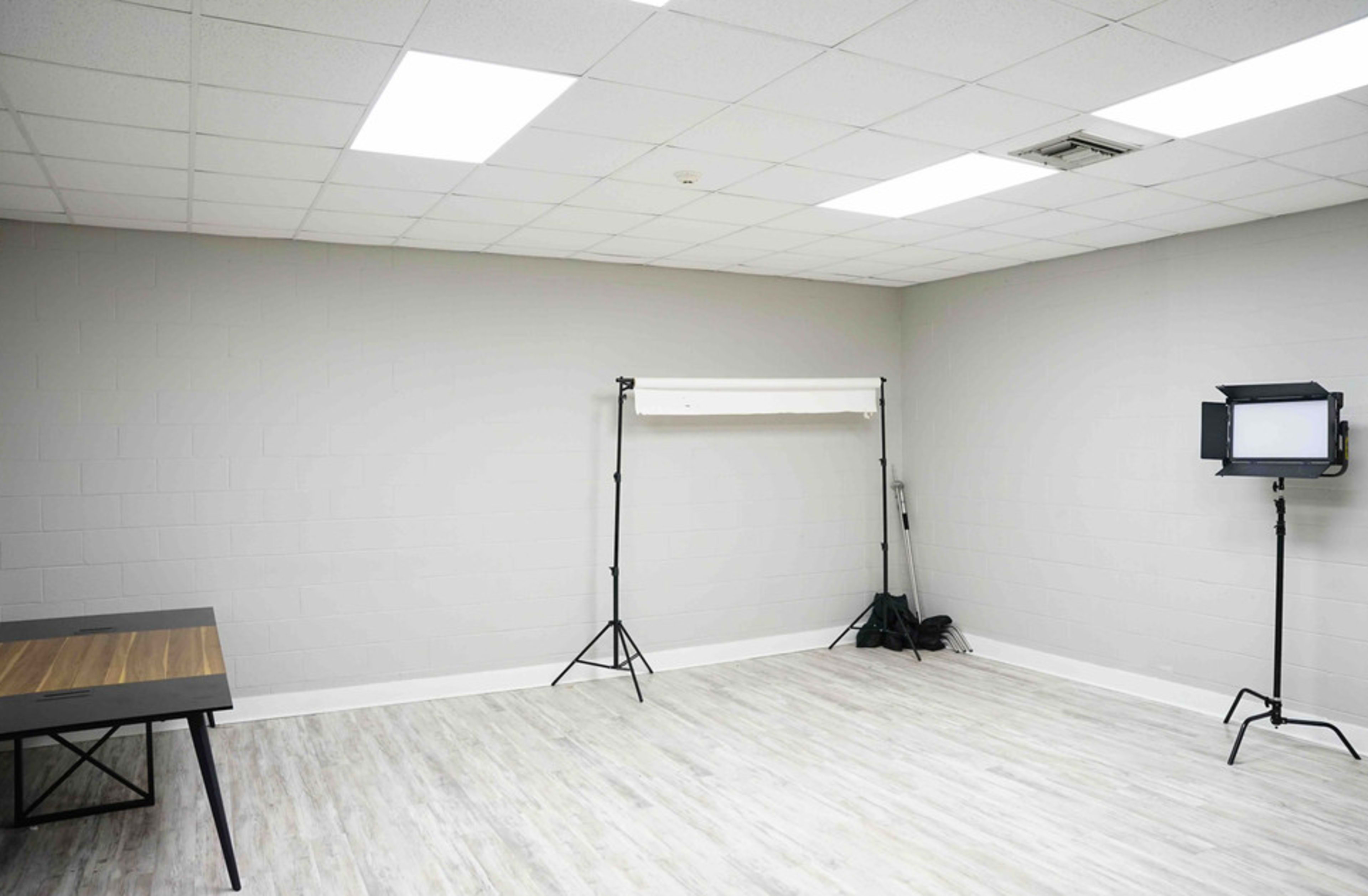 A vacant room with gray walls, a wooden table, a backdrop stand, and a light fixture on tripods.