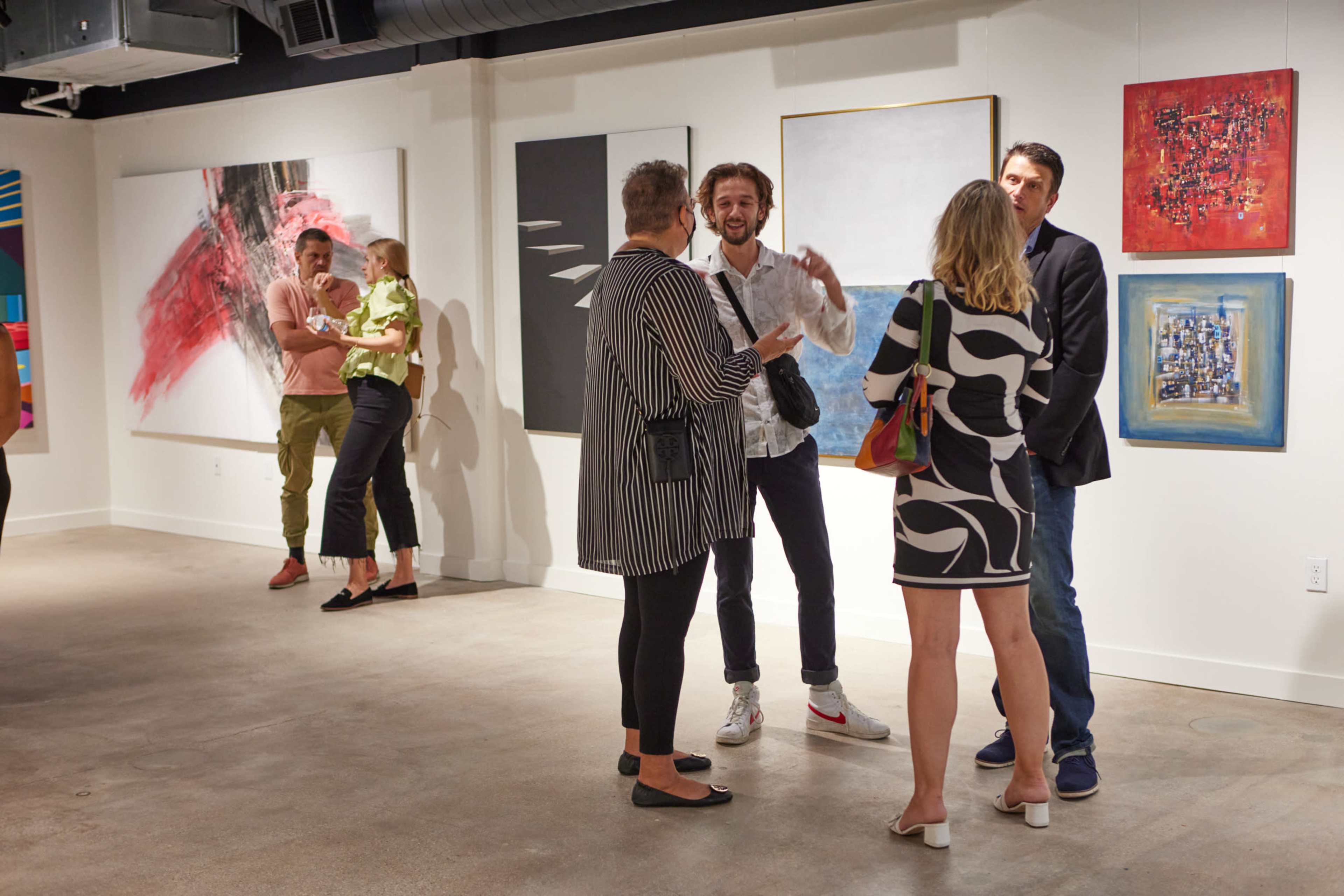 A group of people engages in conversation in an art gallery featuring various artworks on the walls.