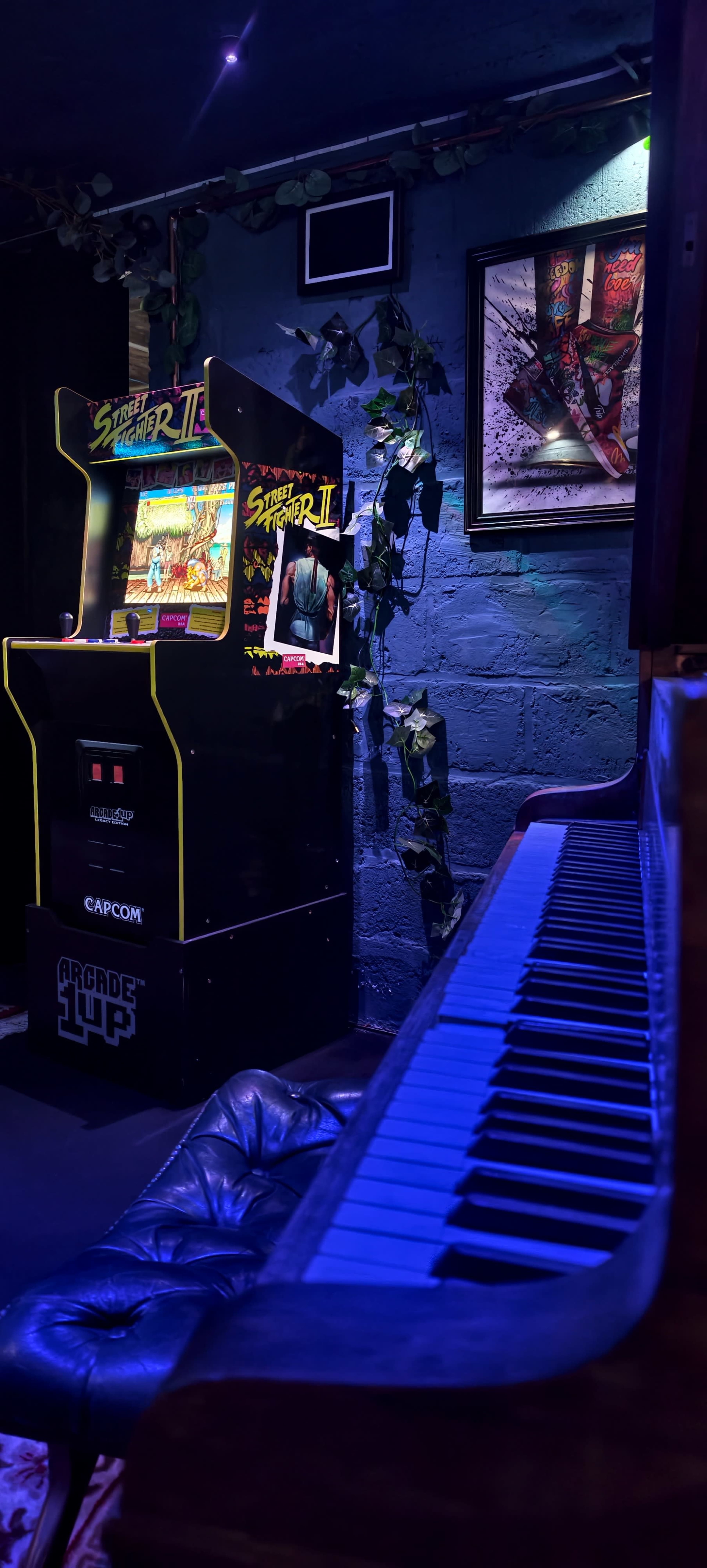 An arcade machine for "Street Fighter II" stands next to a grand piano in a dimly lit room.