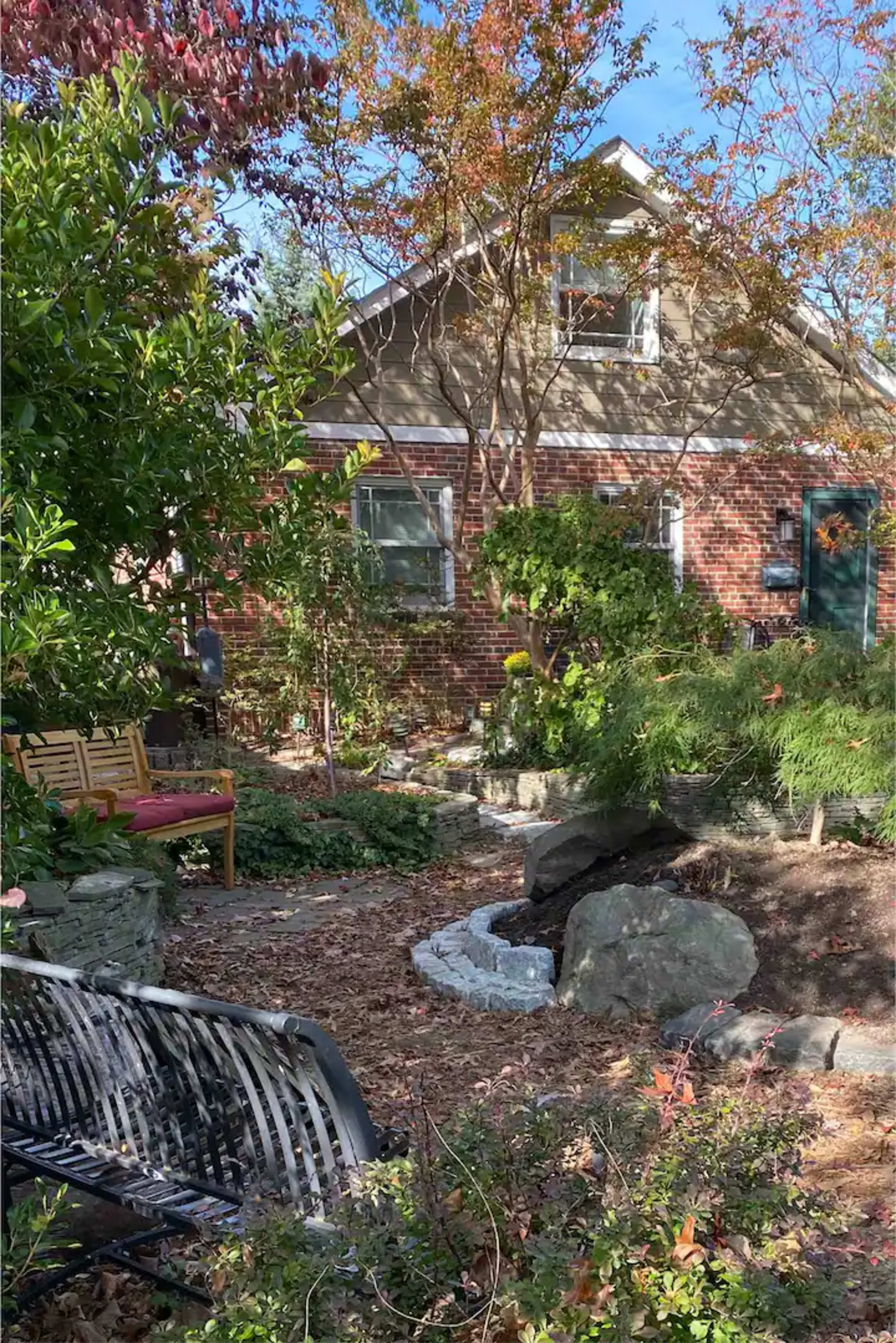 A well-tended garden with a wooden bench, rocks, and various plants in front of a brick house.