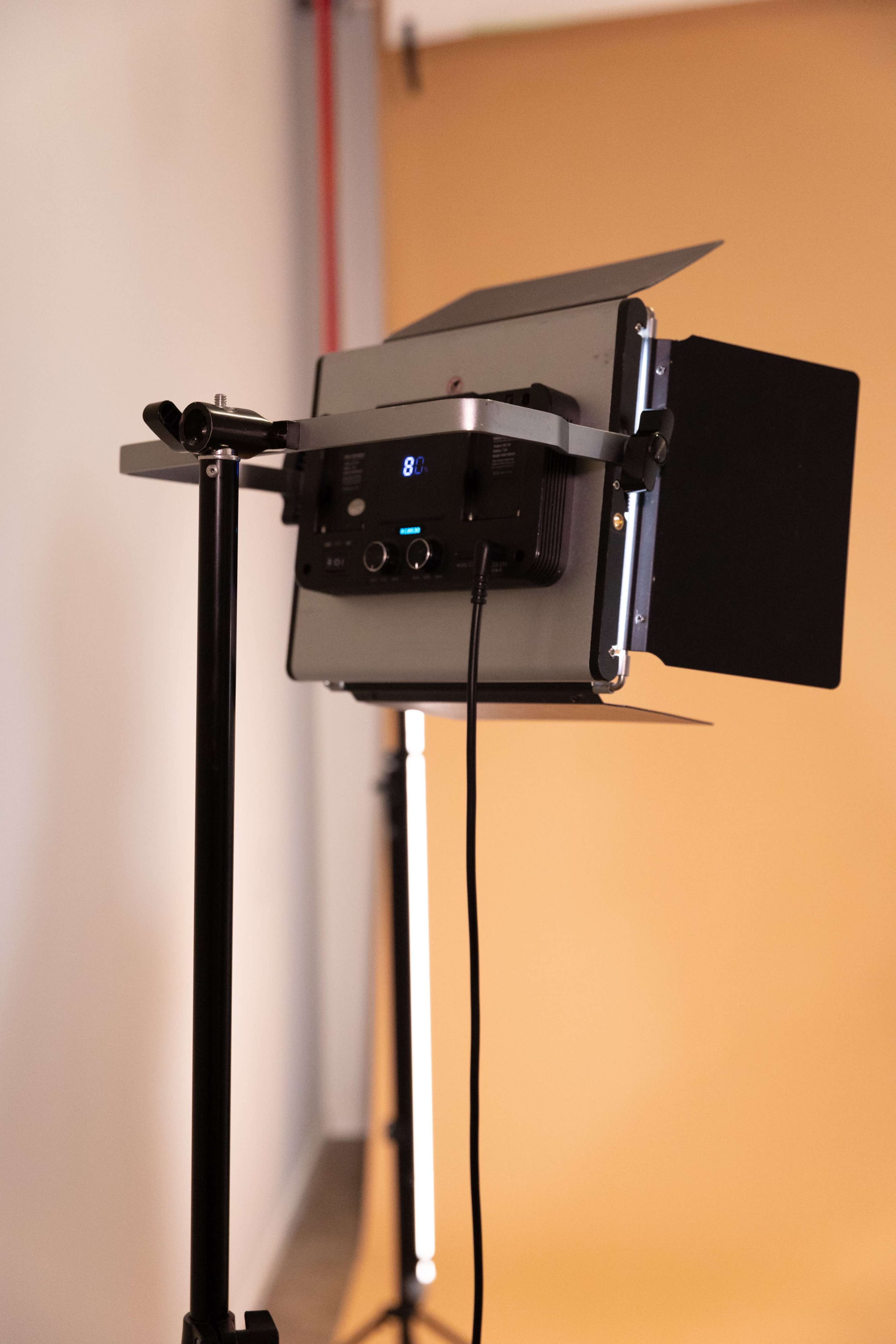 A studio light mounted on a black stand is positioned in front of a beige backdrop.