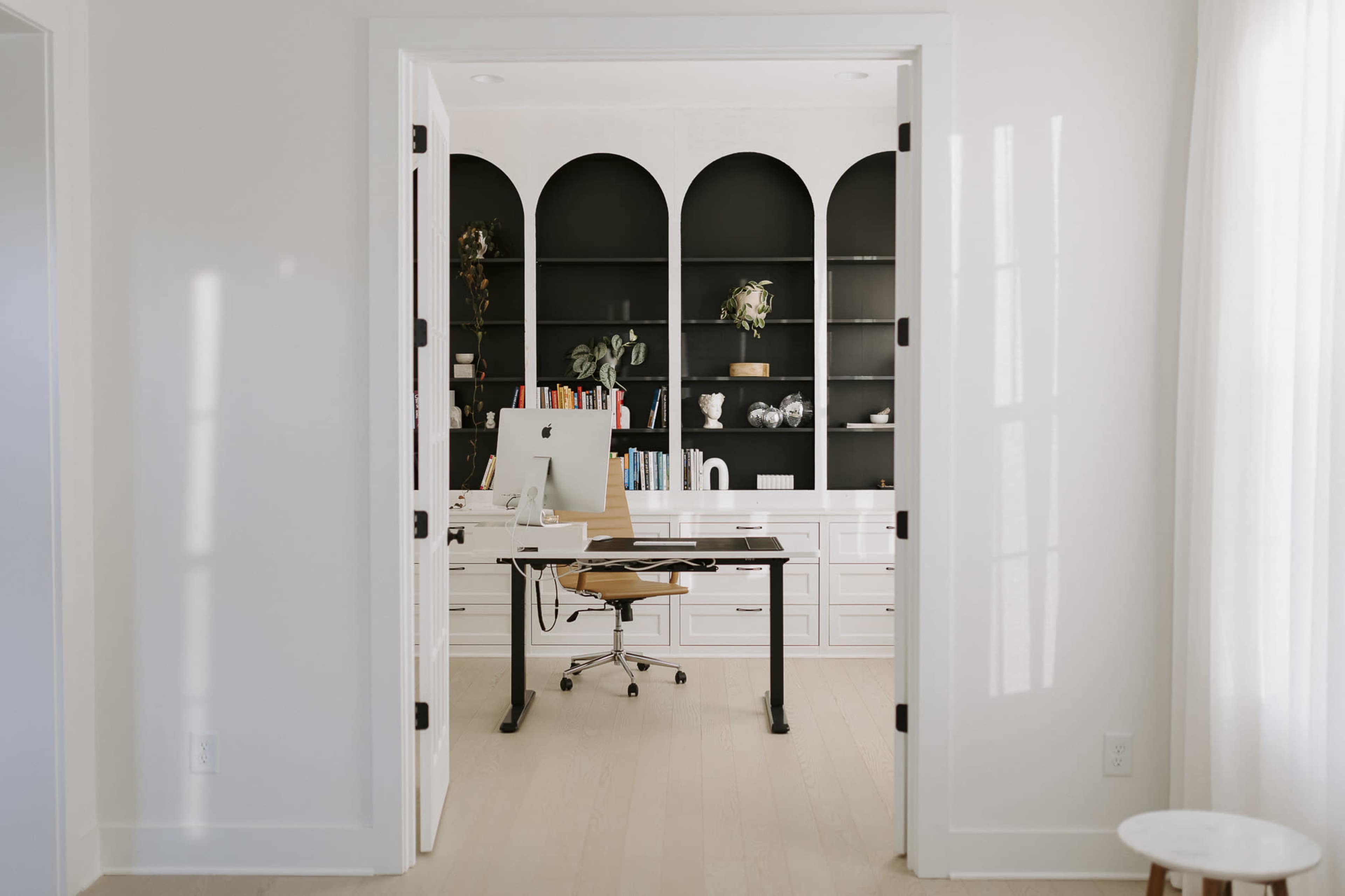 A modern office space is visible through an open doorway, featuring a desk with a computer and a large bookshelf in the background.