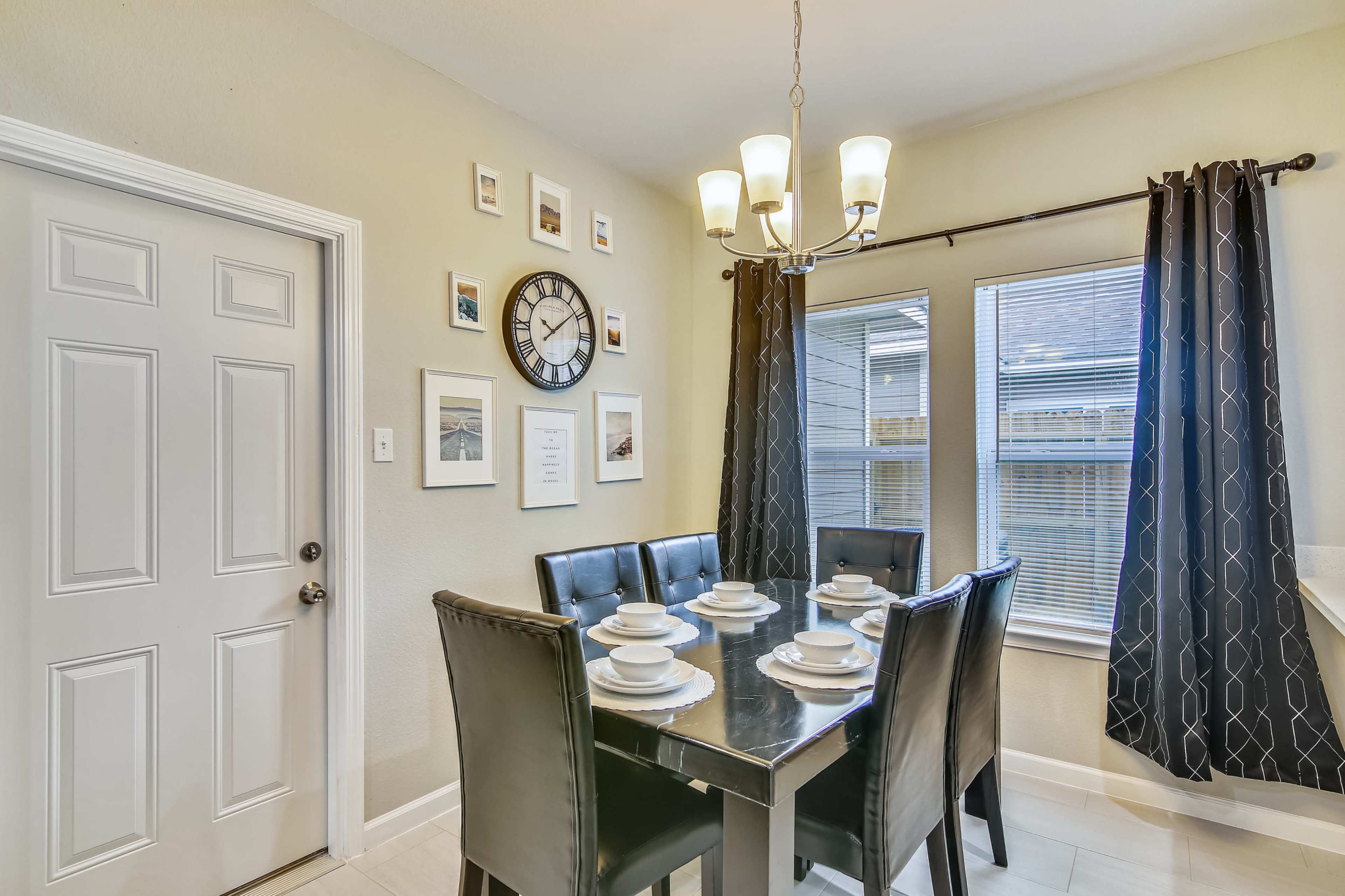 A dining area features a black table set for six, surrounded by leather chairs, with a clock and framed pictures on the wall.