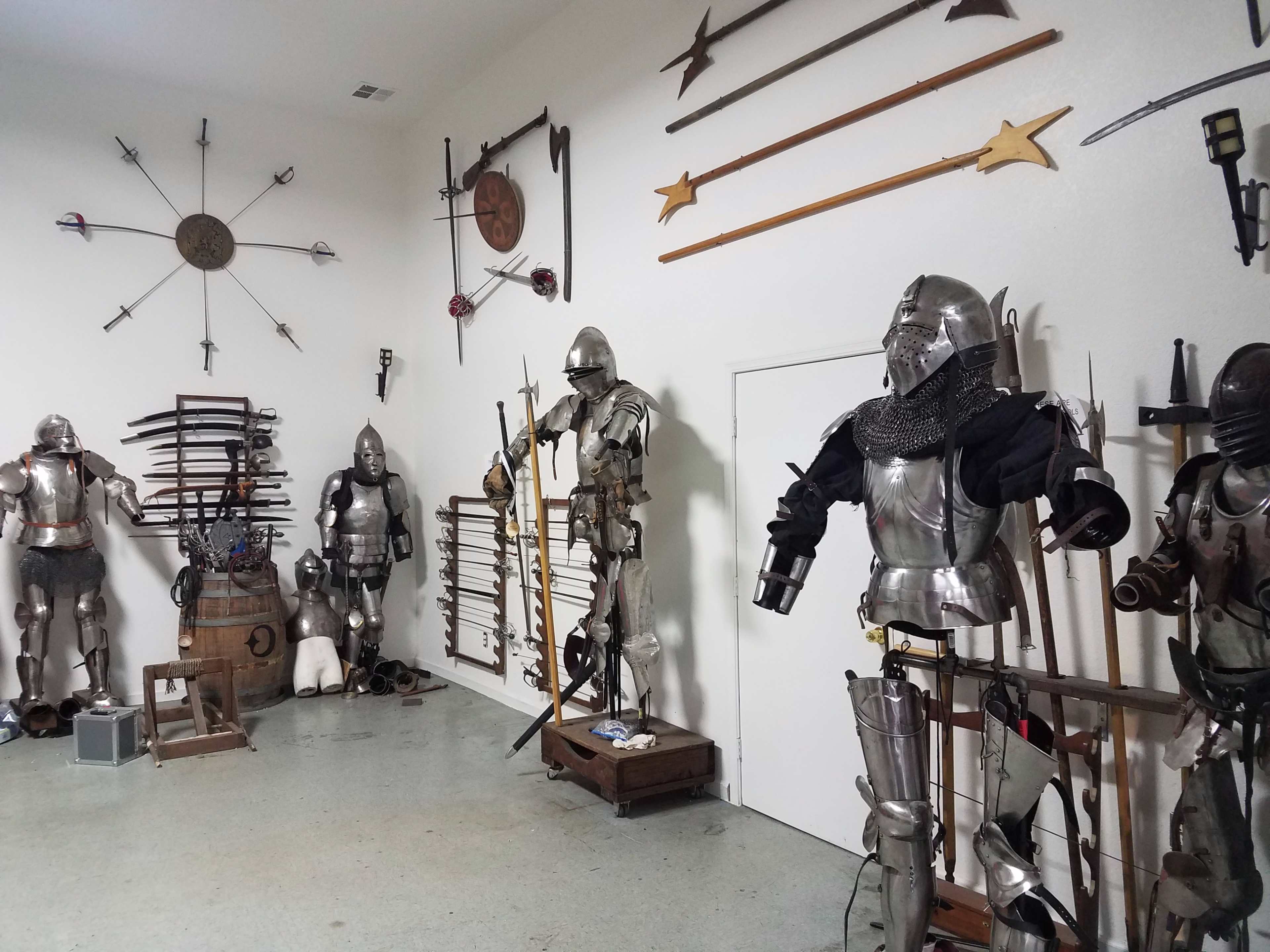 A room filled with various pieces of medieval armor and weapons displayed on stands and mounted on the walls.