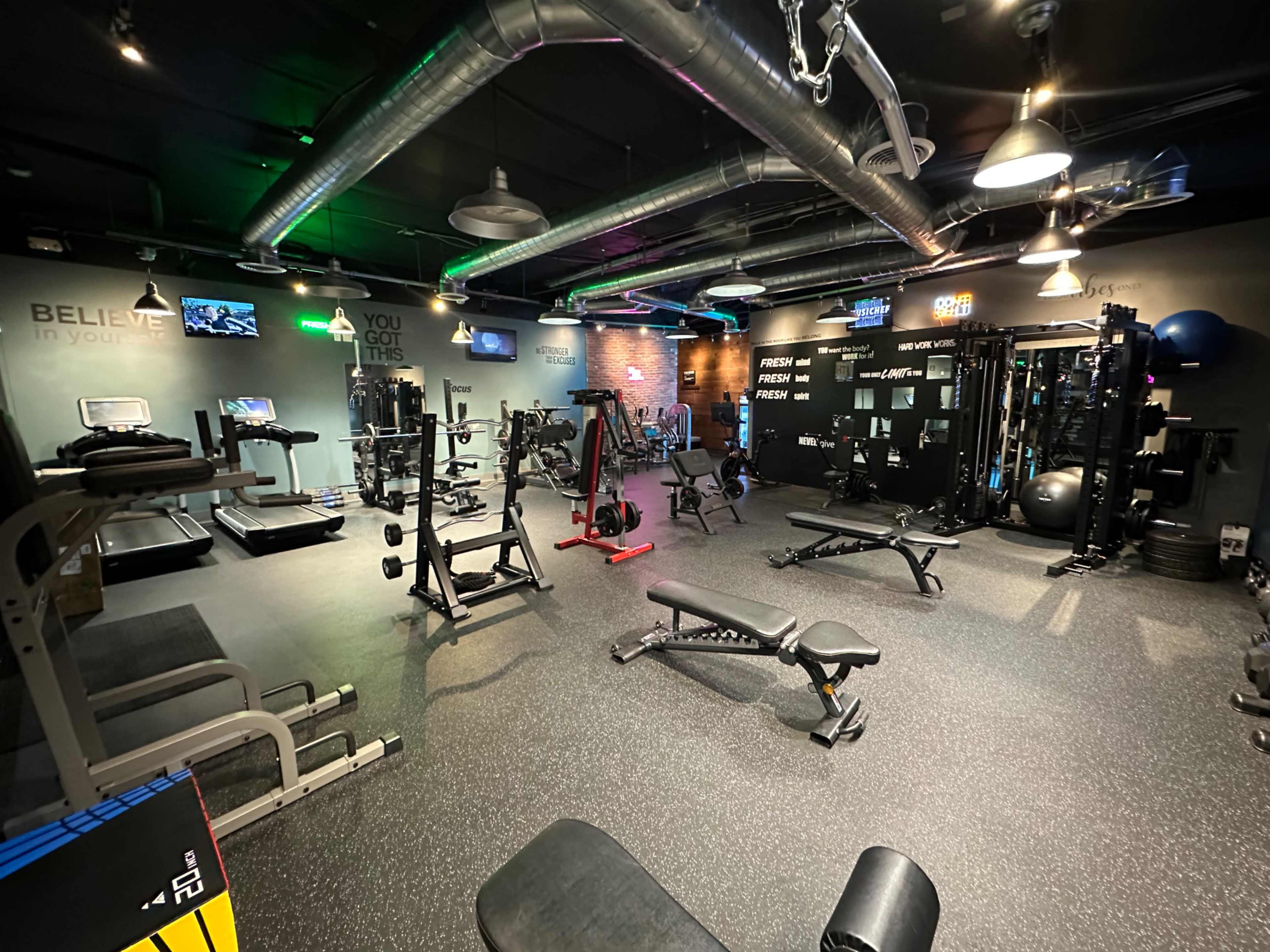 The image shows a well-equipped gym with various exercise machines and weights displayed in a spacious room.