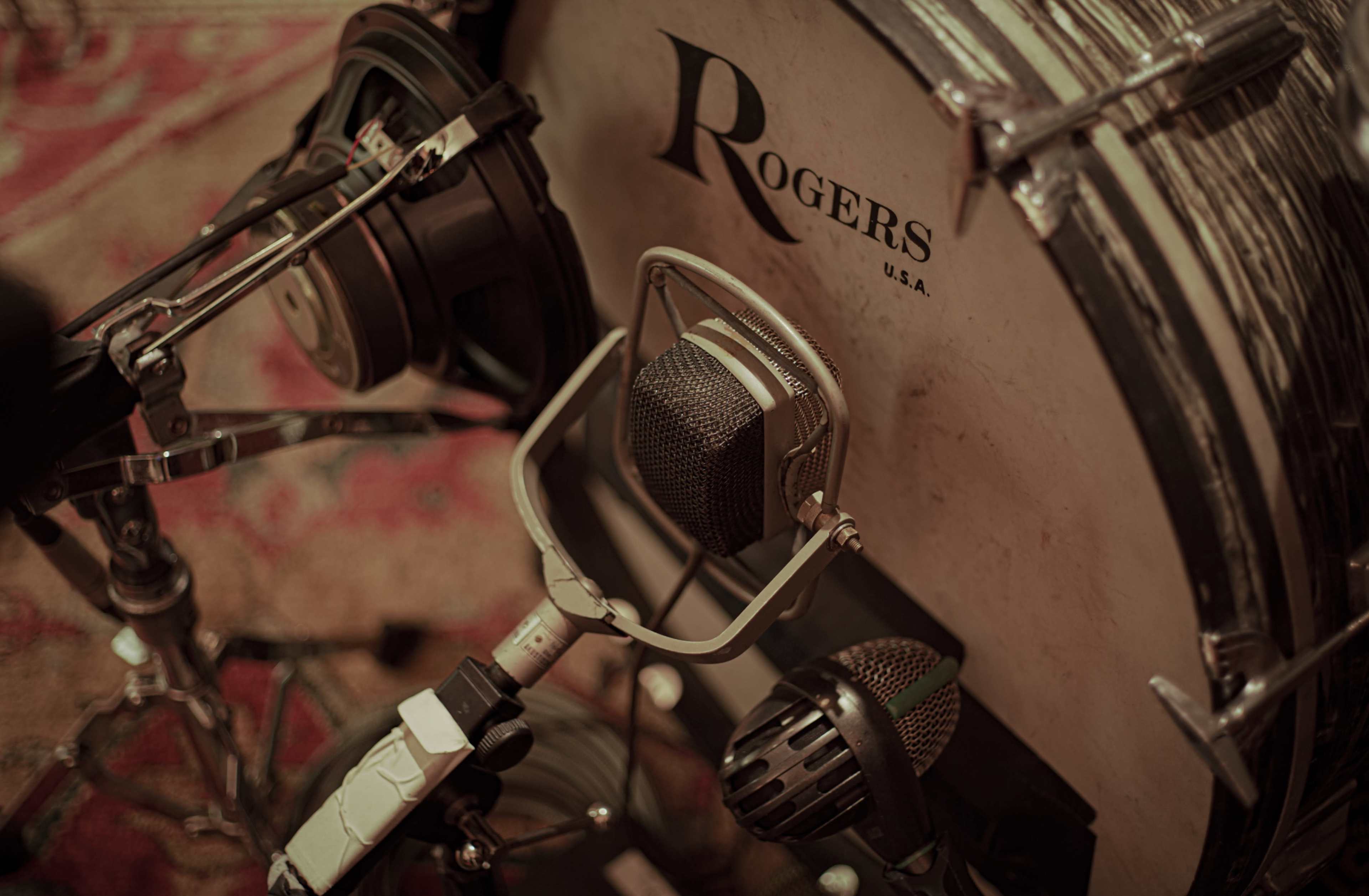 The image features a close-up of a drum kit with various microphones positioned near the bass drum.
