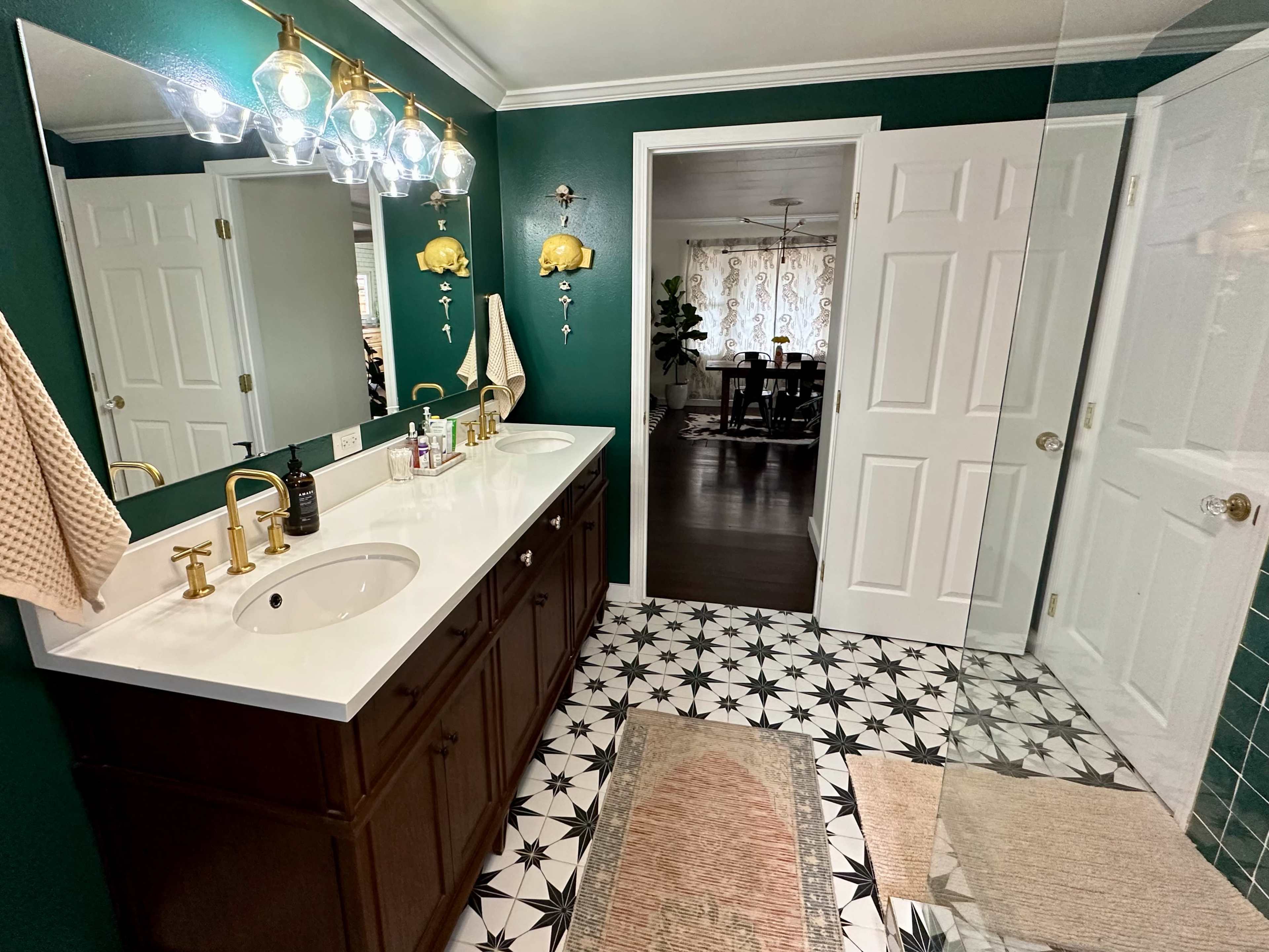 The image shows a bathroom featuring a double sink vanity with dark cabinetry, a green wall, and hexagonal patterned floor tiles.