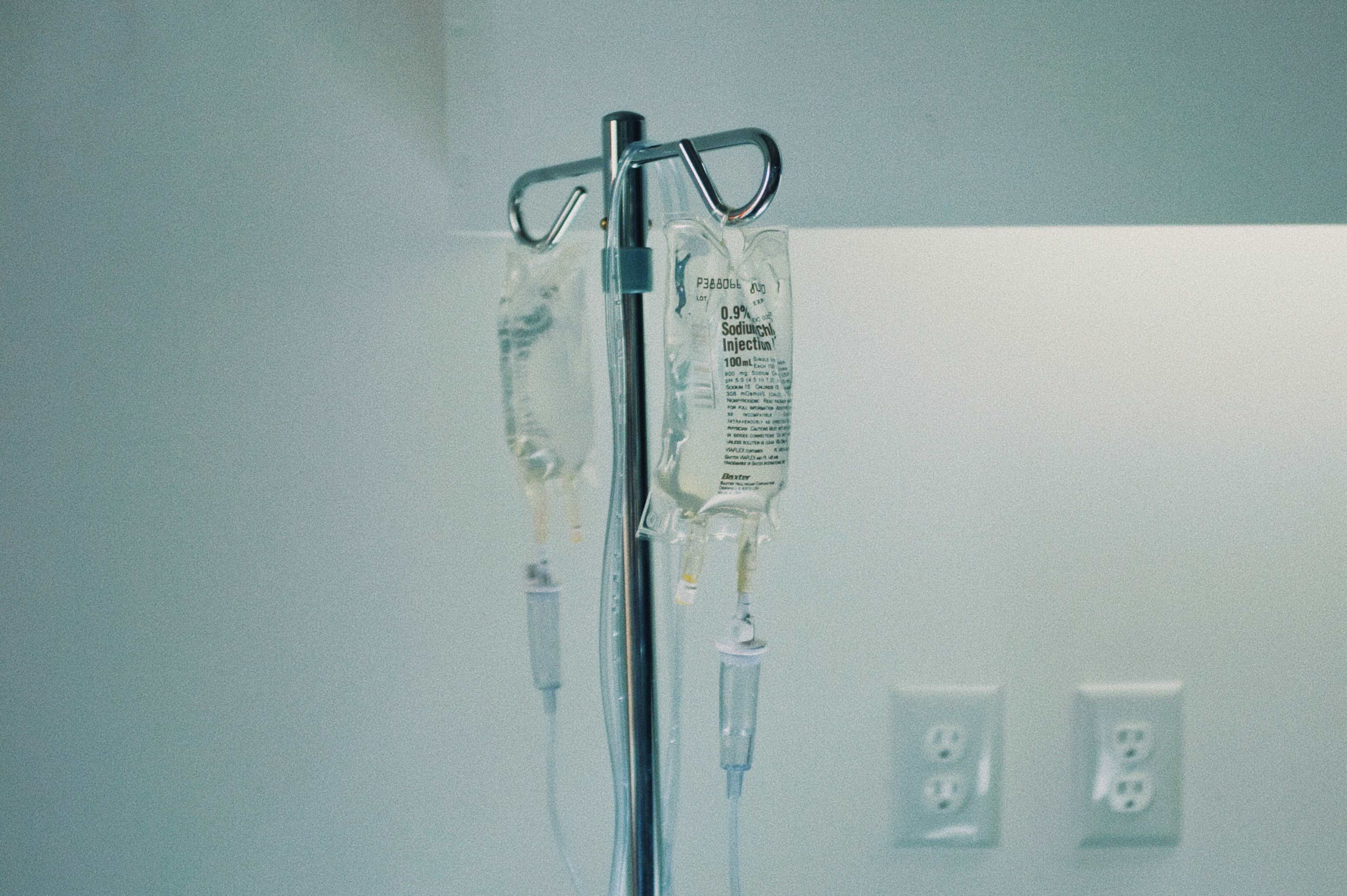 An intravenous drip stand holds two bags of fluid in a medical setting.