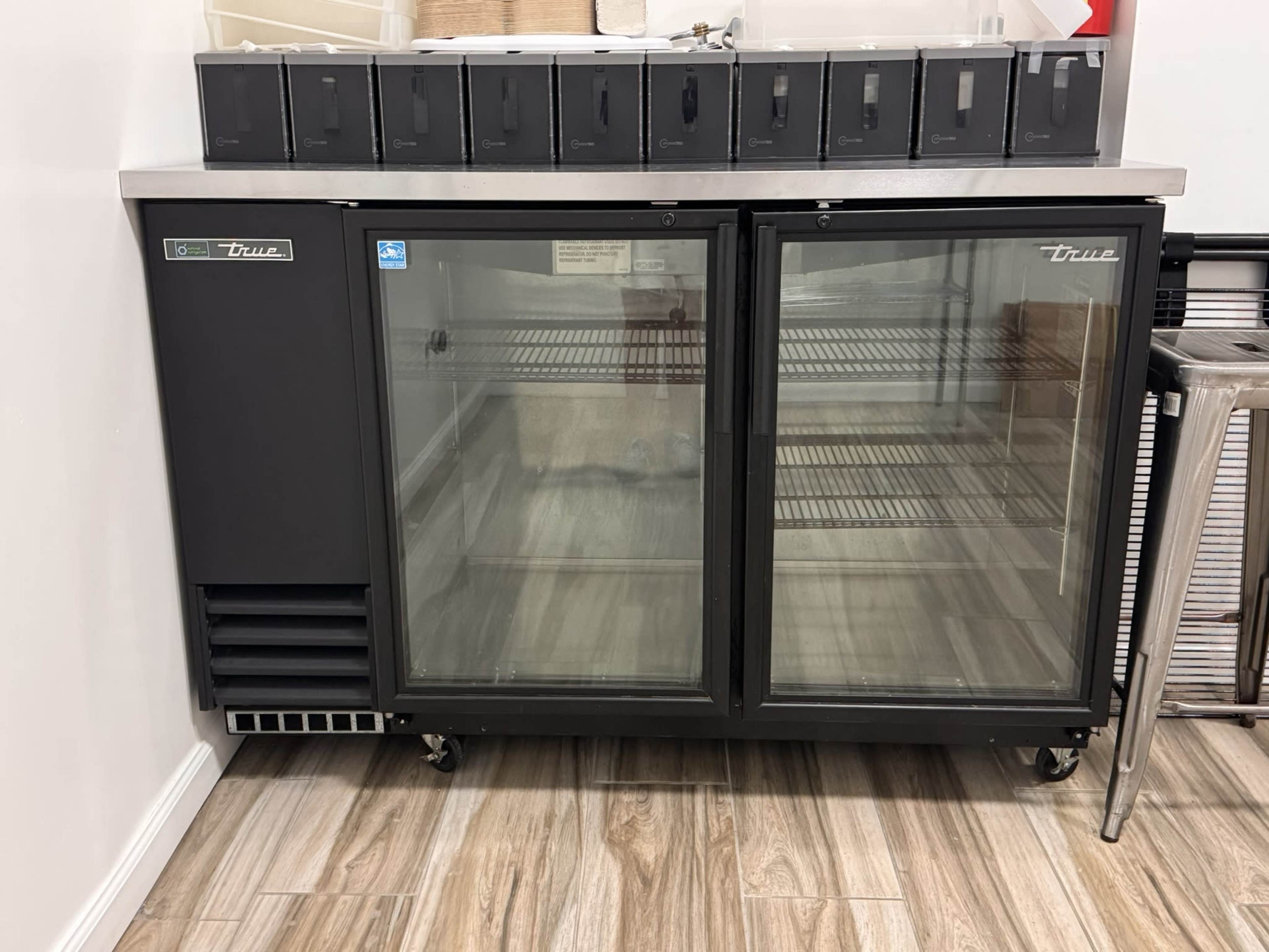 A commercial refrigerator with glass doors is positioned against a wall, displaying empty shelves inside.