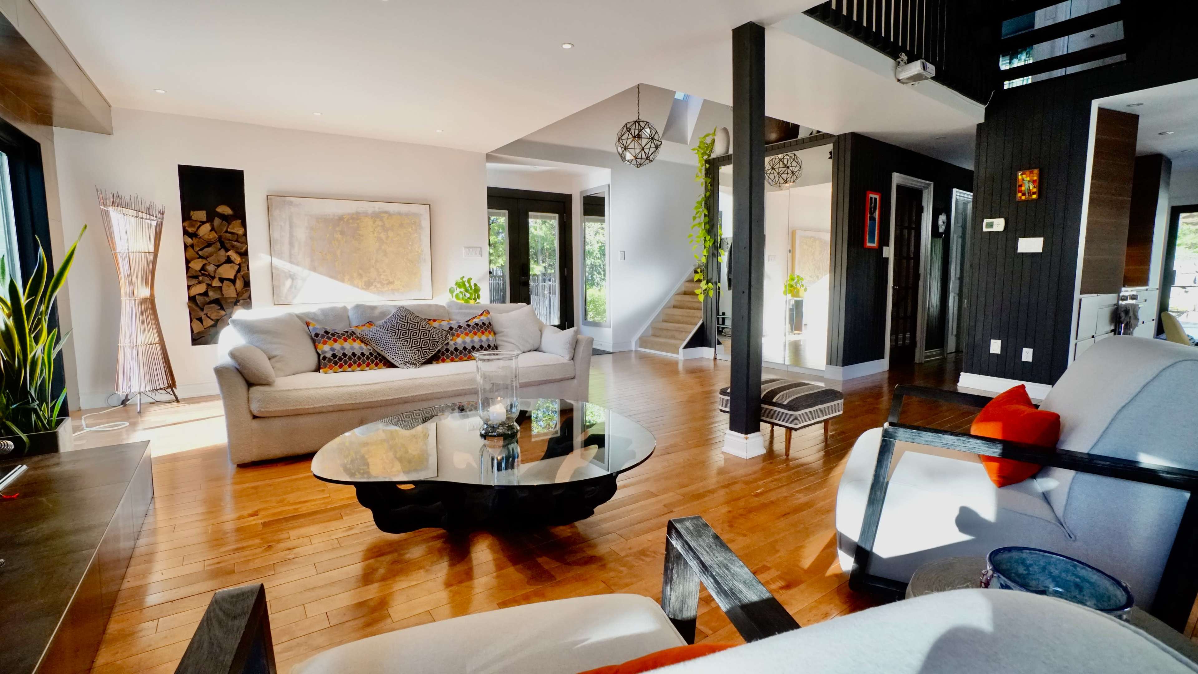 A spacious living room with wooden floors, modern furniture, and large windows letting in natural light.