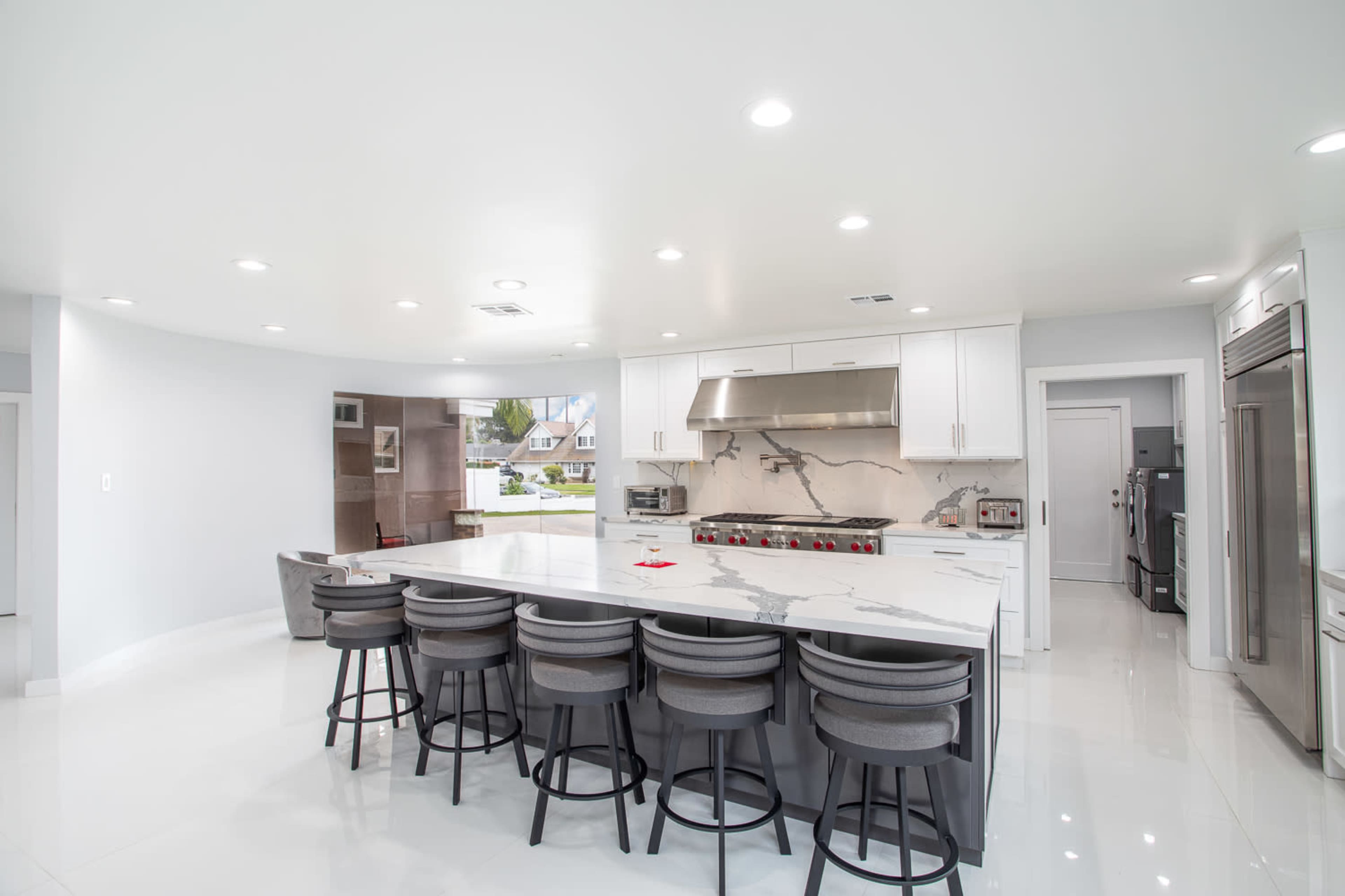 A modern kitchen featuring a large marble-topped island with seating, stainless steel appliances, and sleek white cabinetry.