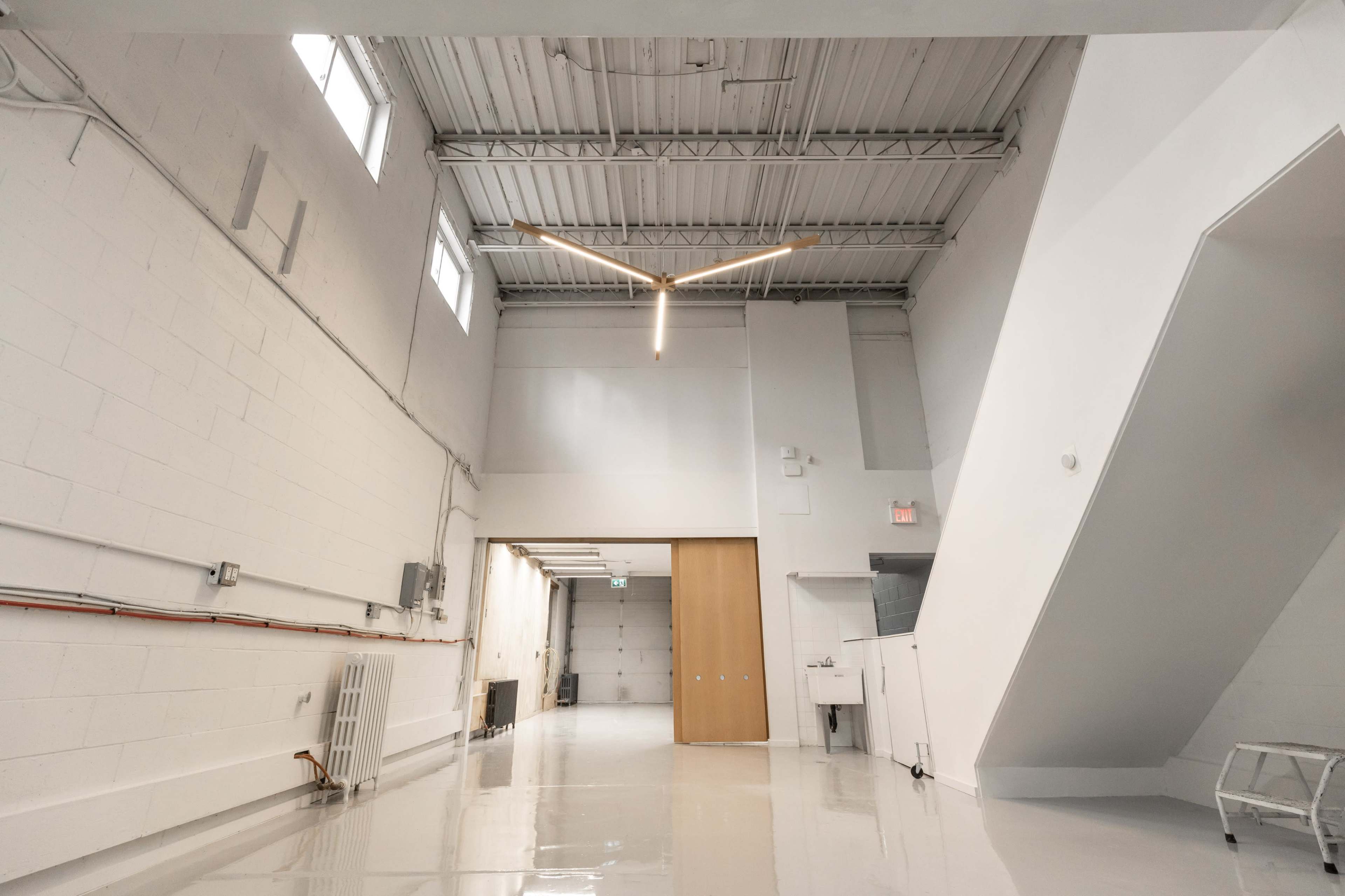 The image features a spacious, minimalistic interior with white walls, a high ceiling, and a staircase in the corner.