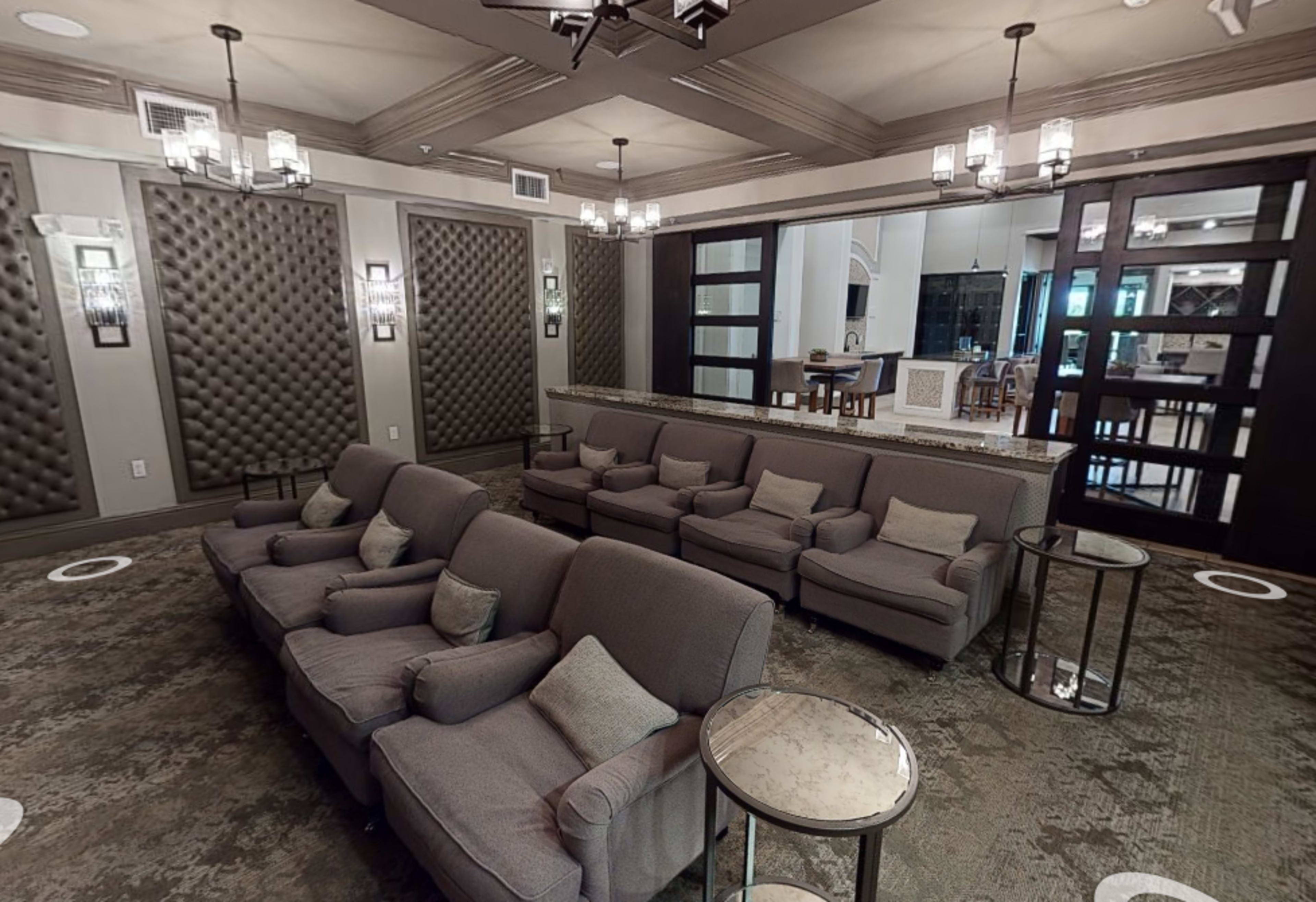 A lounge area with several gray sofas arranged around small tables, set against a backdrop of textured wall panels and pendant lighting.
