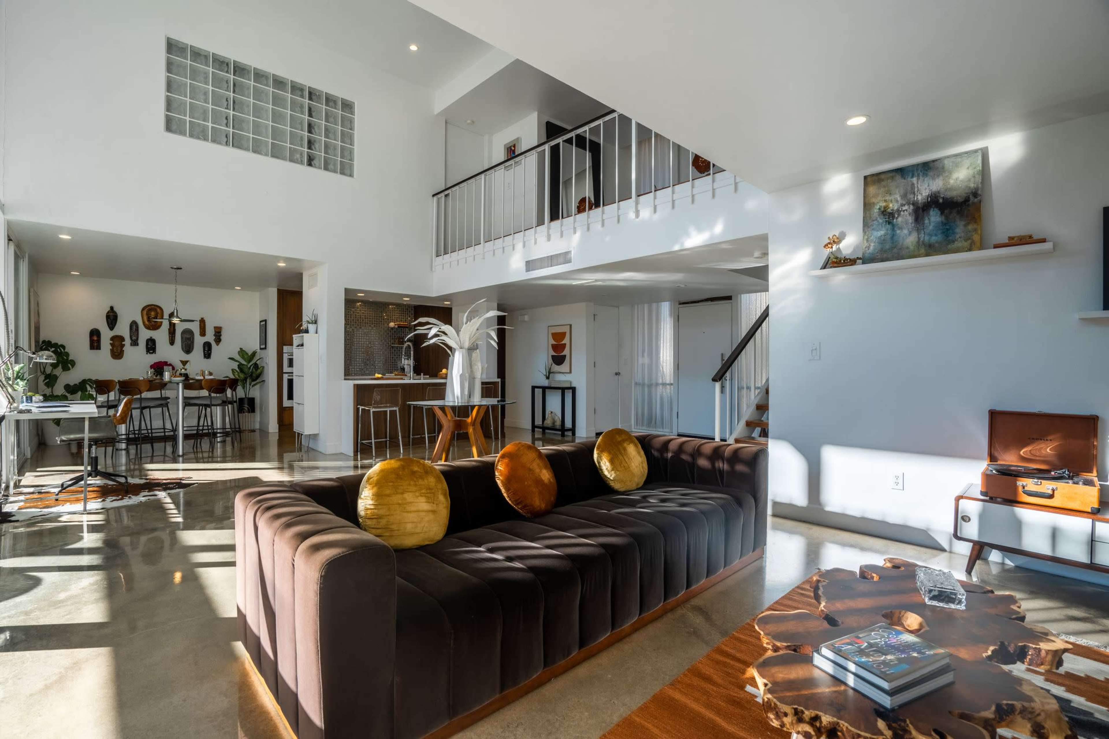 A modern living room with a dark sofa, wooden coffee table, and an open layout that connects to a dining area and kitchen.