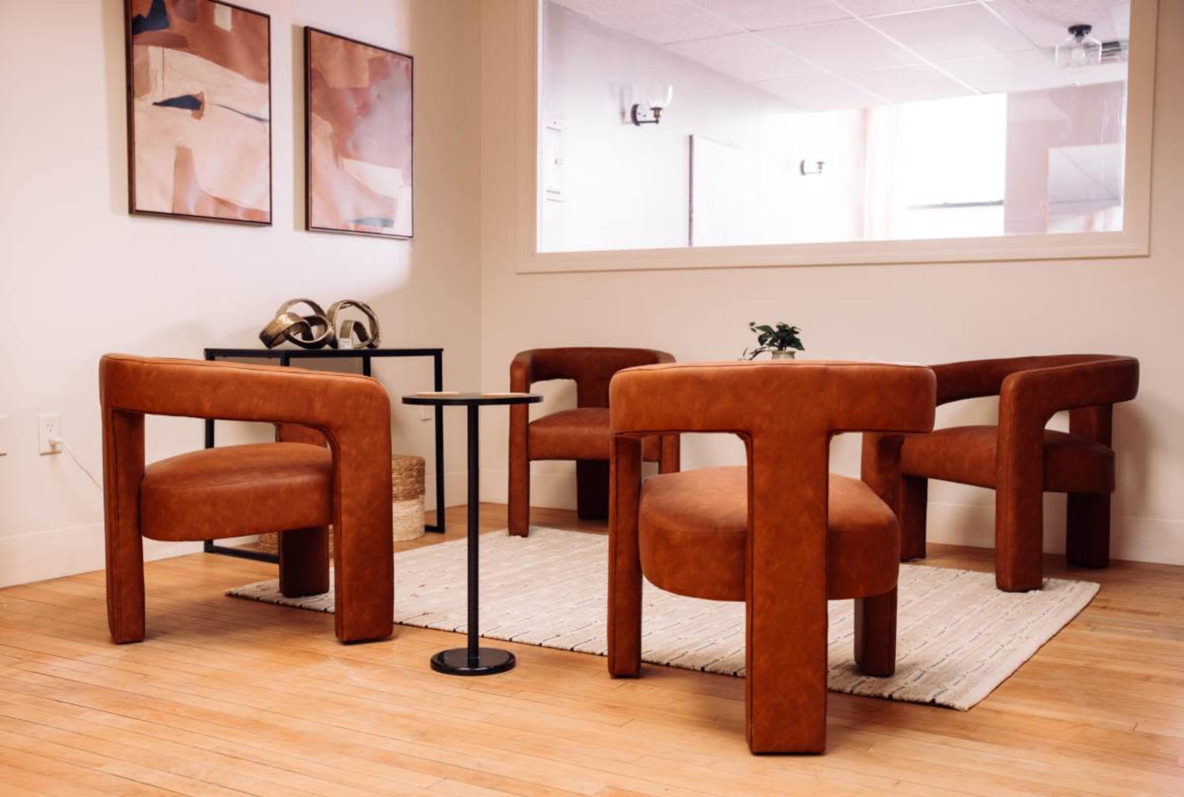 The image shows a modern seating area with four brown leather chairs arranged around a small black side table on a light wooden floor.