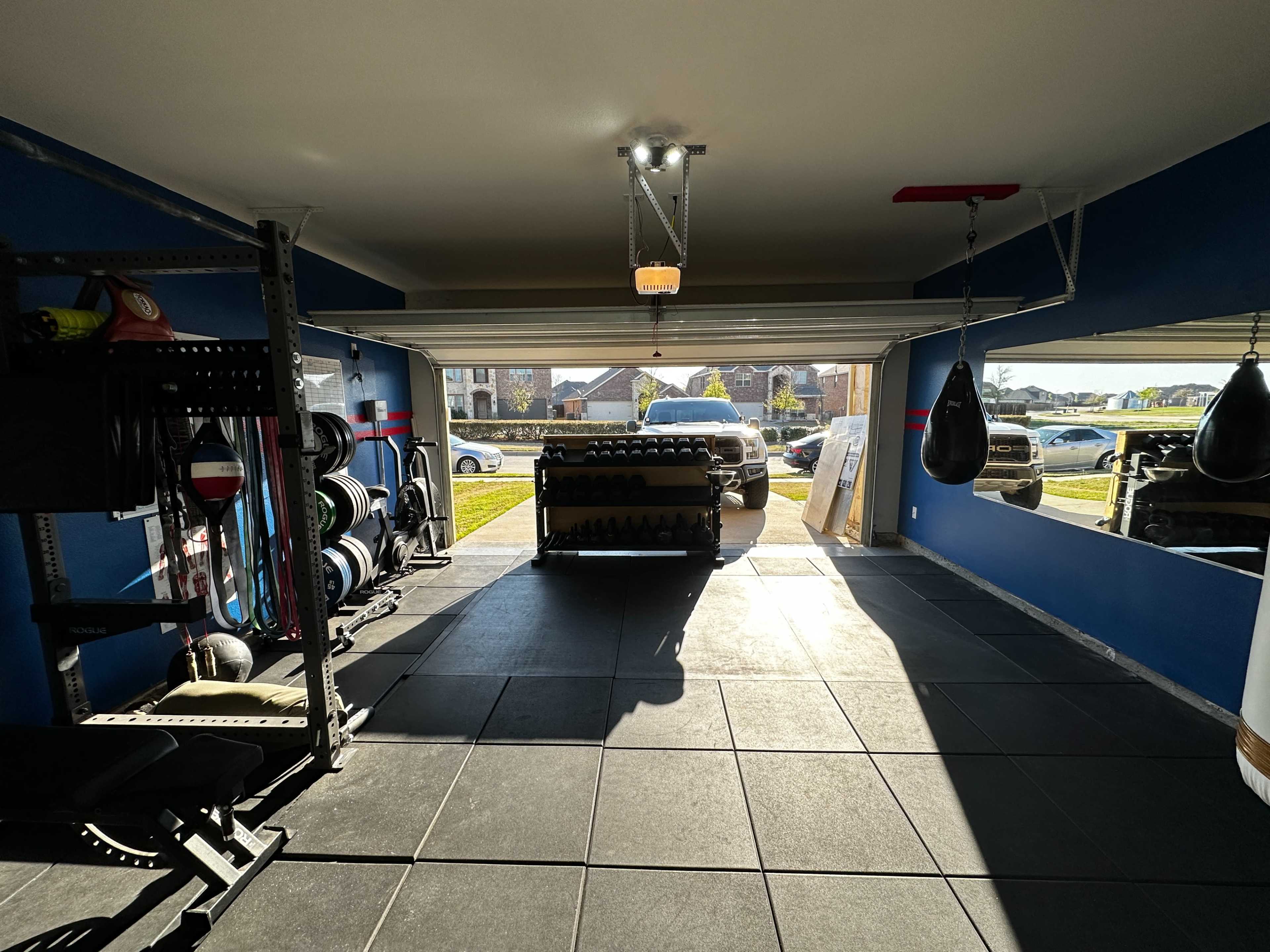 A garage gym equipped with weights, a punching bag, and large windows allowing natural light to enter.