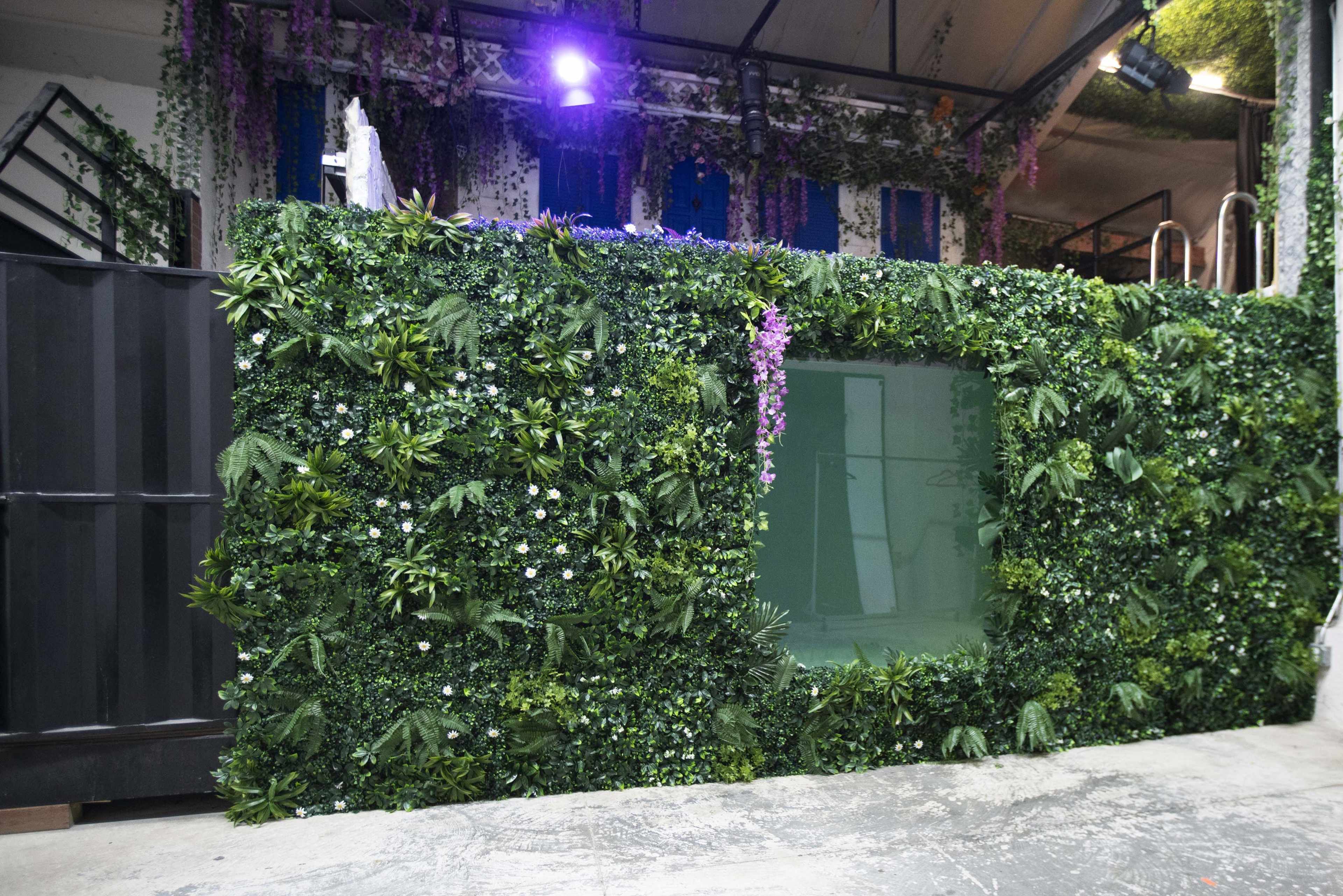 A green wall covered in artificial foliage and flowers, with a transparent window in the center.