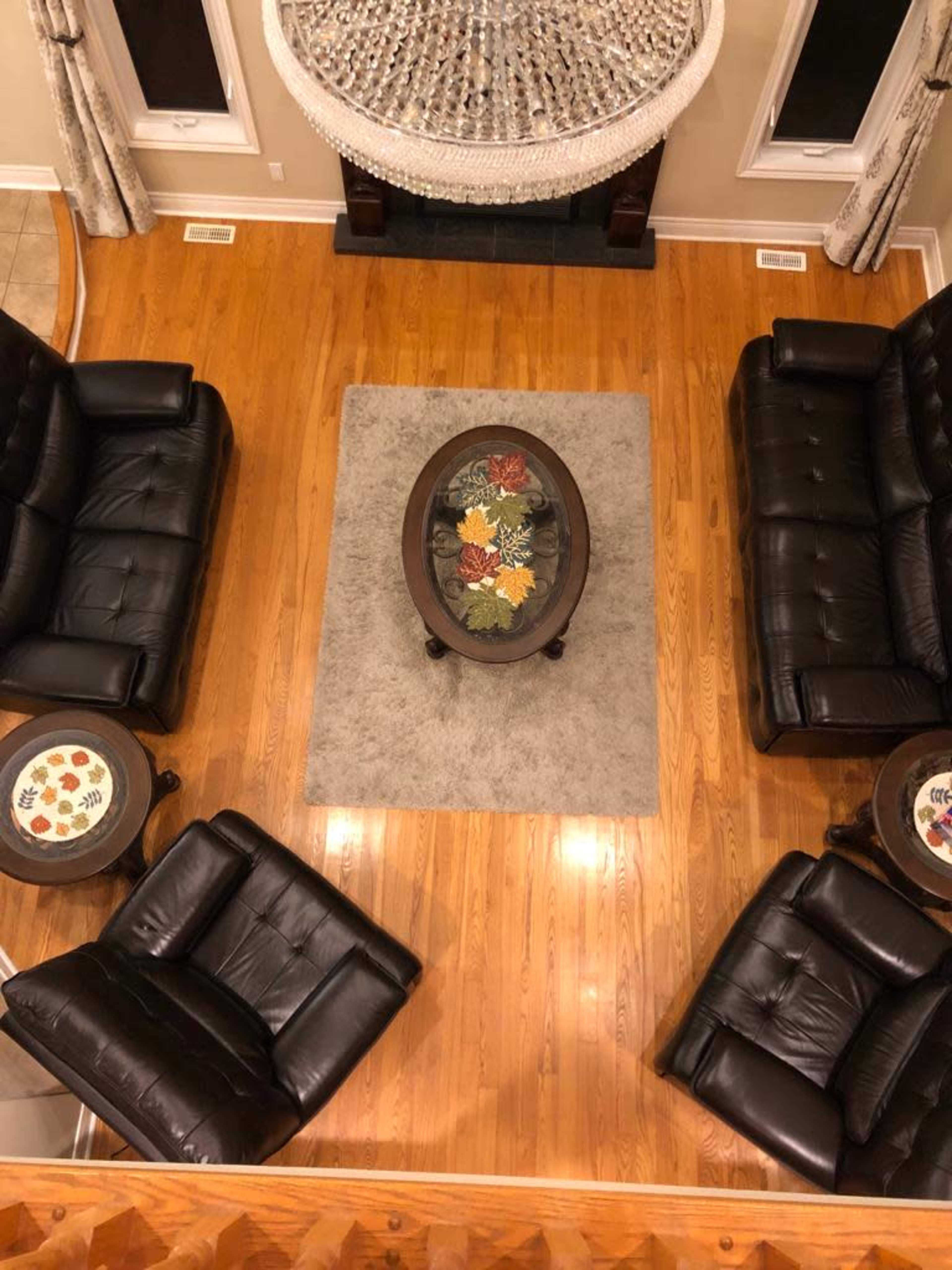 A living room with dark leather sofas arranged around a circular coffee table, placed on a light area rug on a wooden floor.