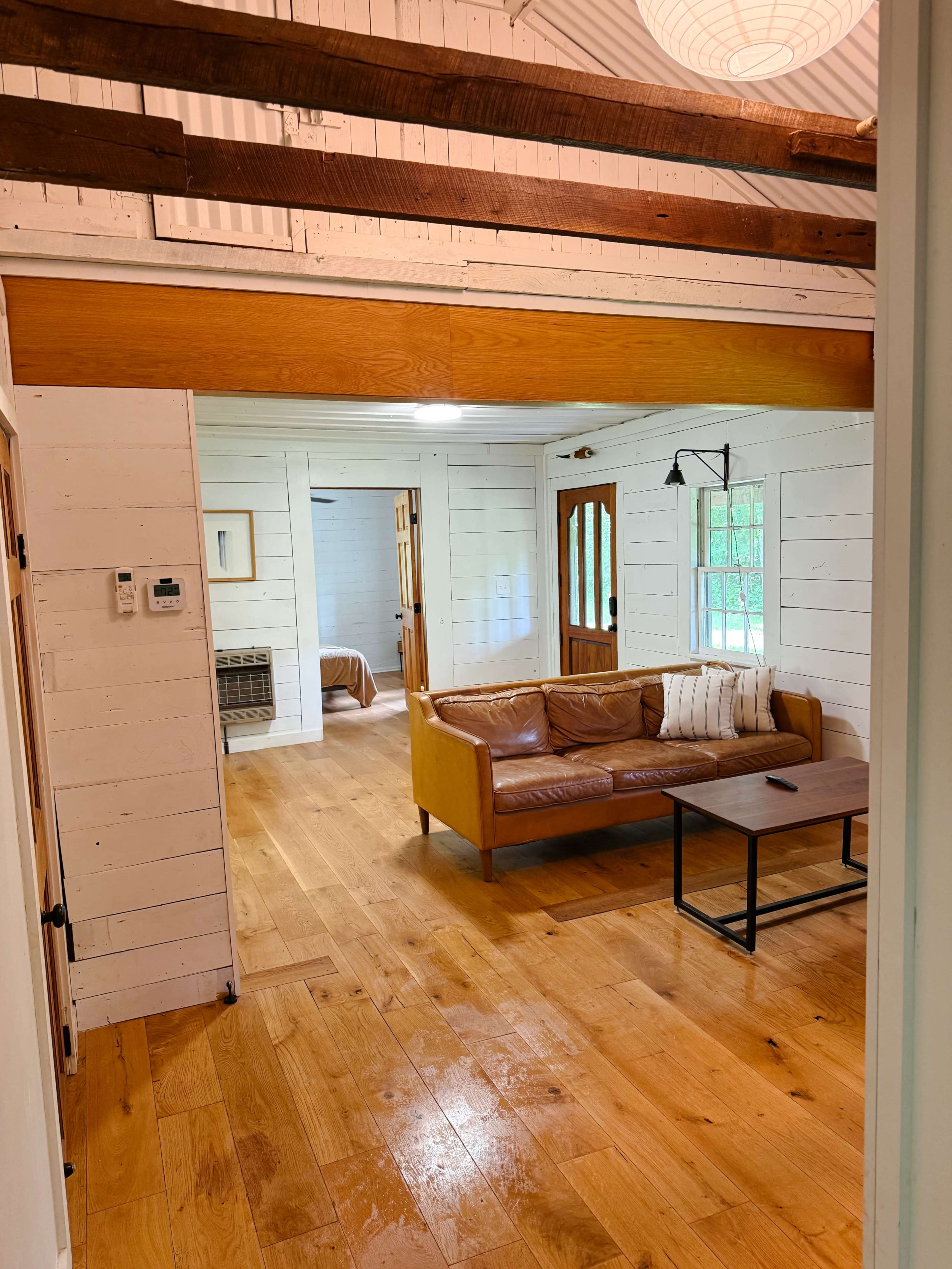 The image shows a cozy interior of a house featuring a brown leather couch, a wooden coffee table, and white-paneled walls.