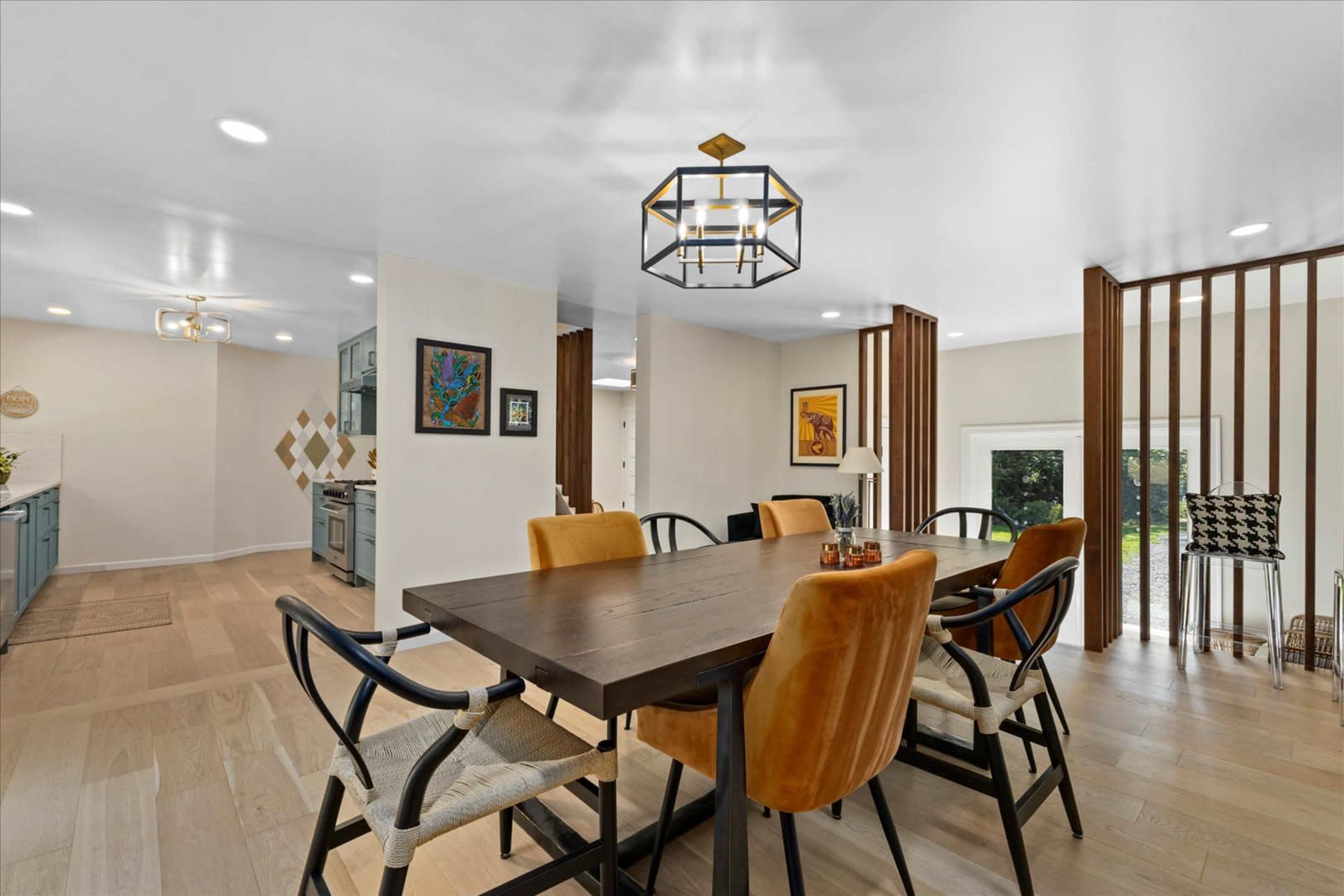 The image shows a modern dining area featuring a wooden table surrounded by upholstered chairs, with light-colored walls and decorative accents.