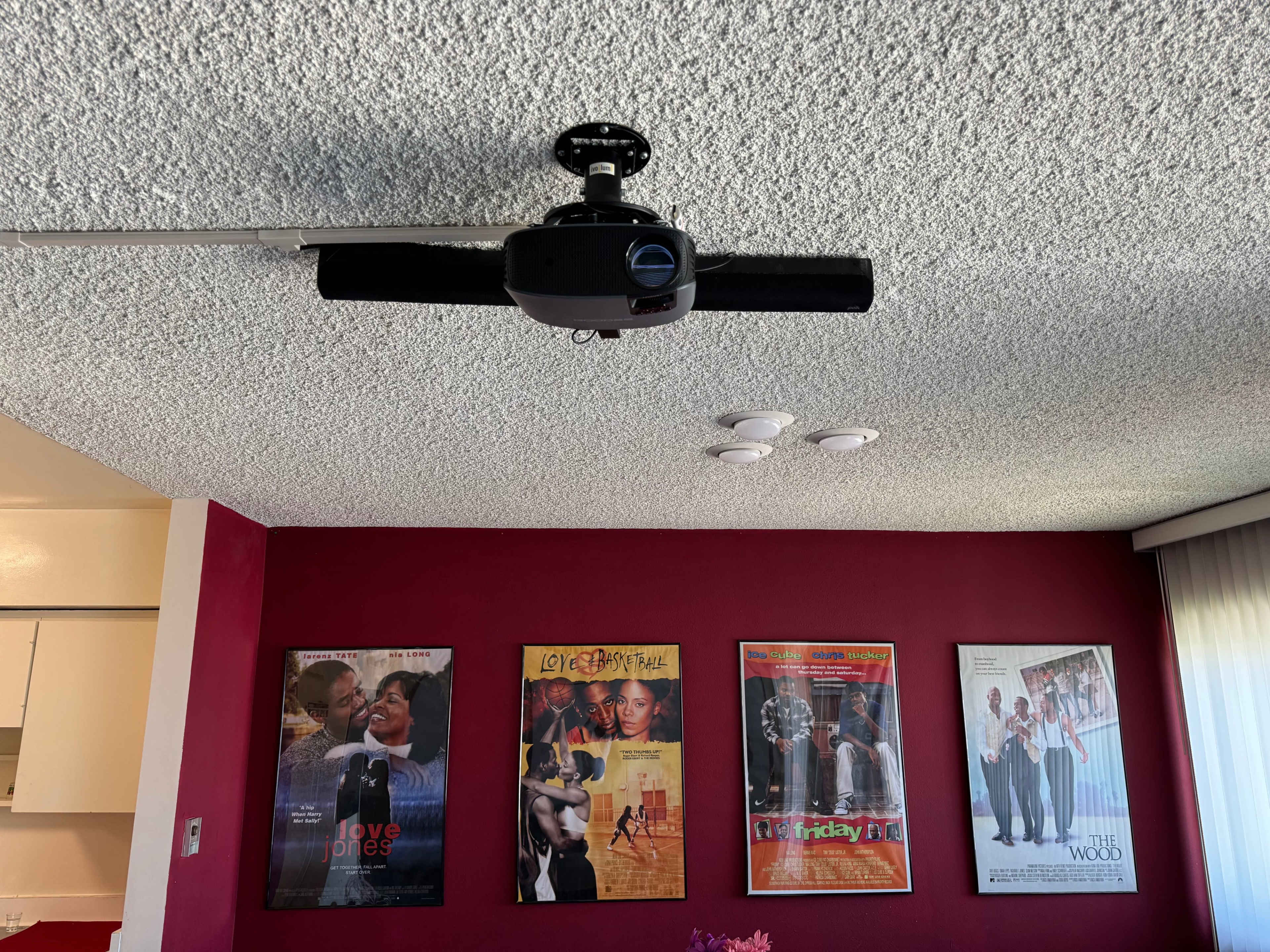 A ceiling fan mounted on a textured ceiling, with several movie posters displayed on a red wall.