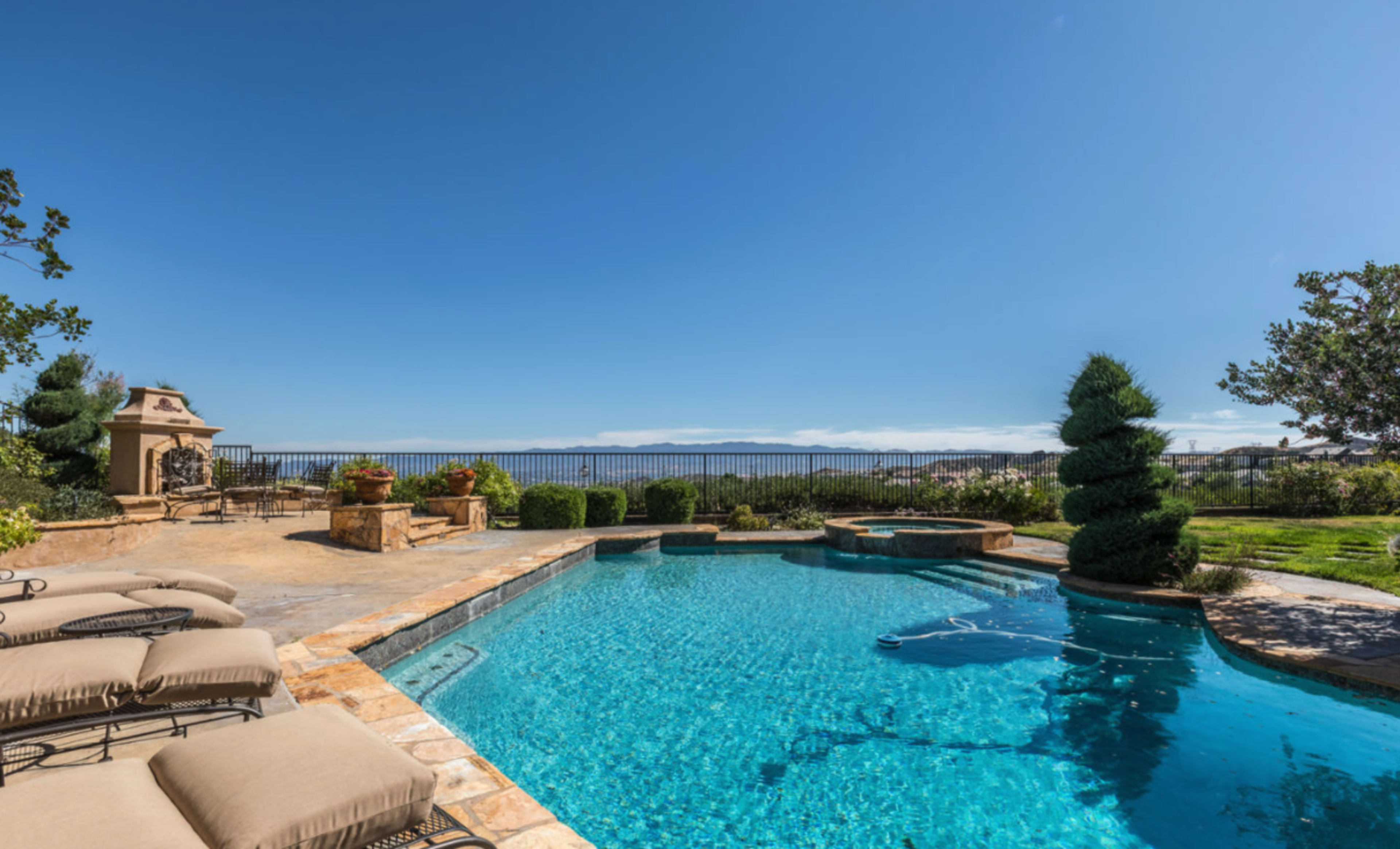 A landscaped backyard features a swimming pool with lounge chairs and a view of distant hills.