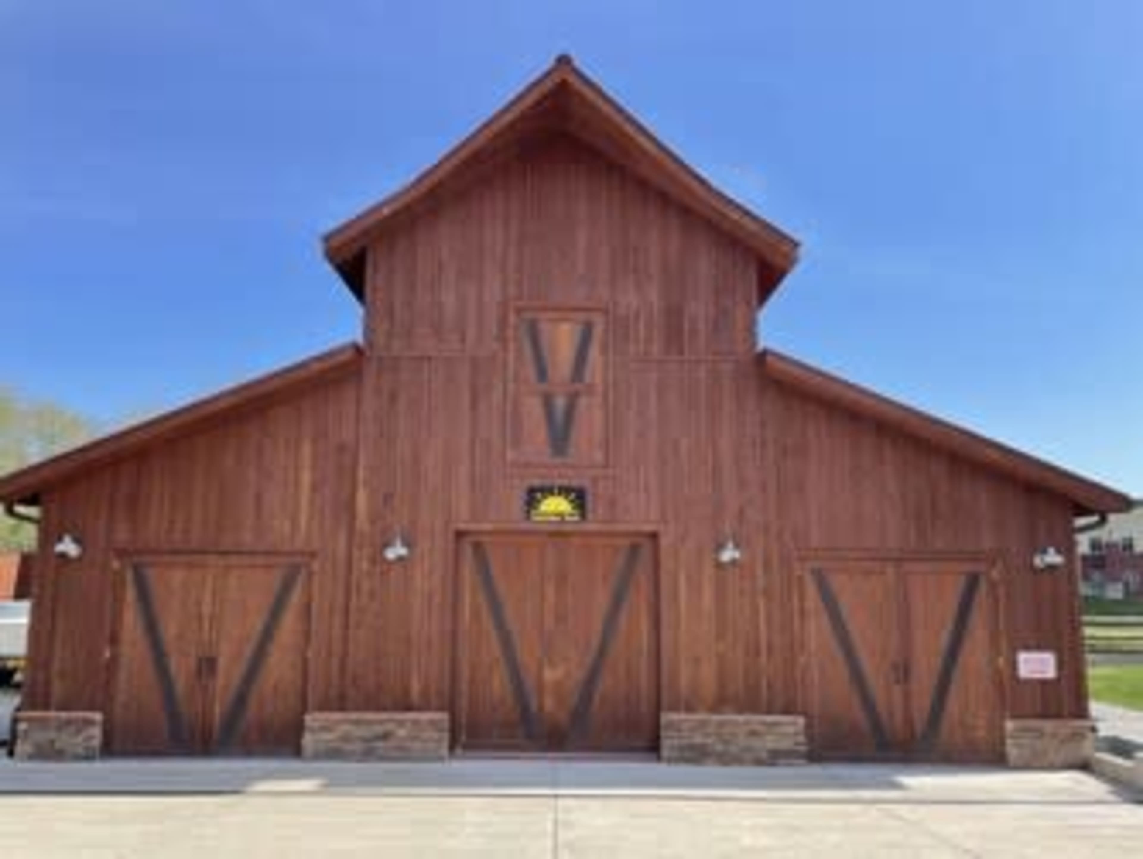 The image shows a large wooden barn with a pointed roof and two wide doors at the front, set against a clear blue sky.