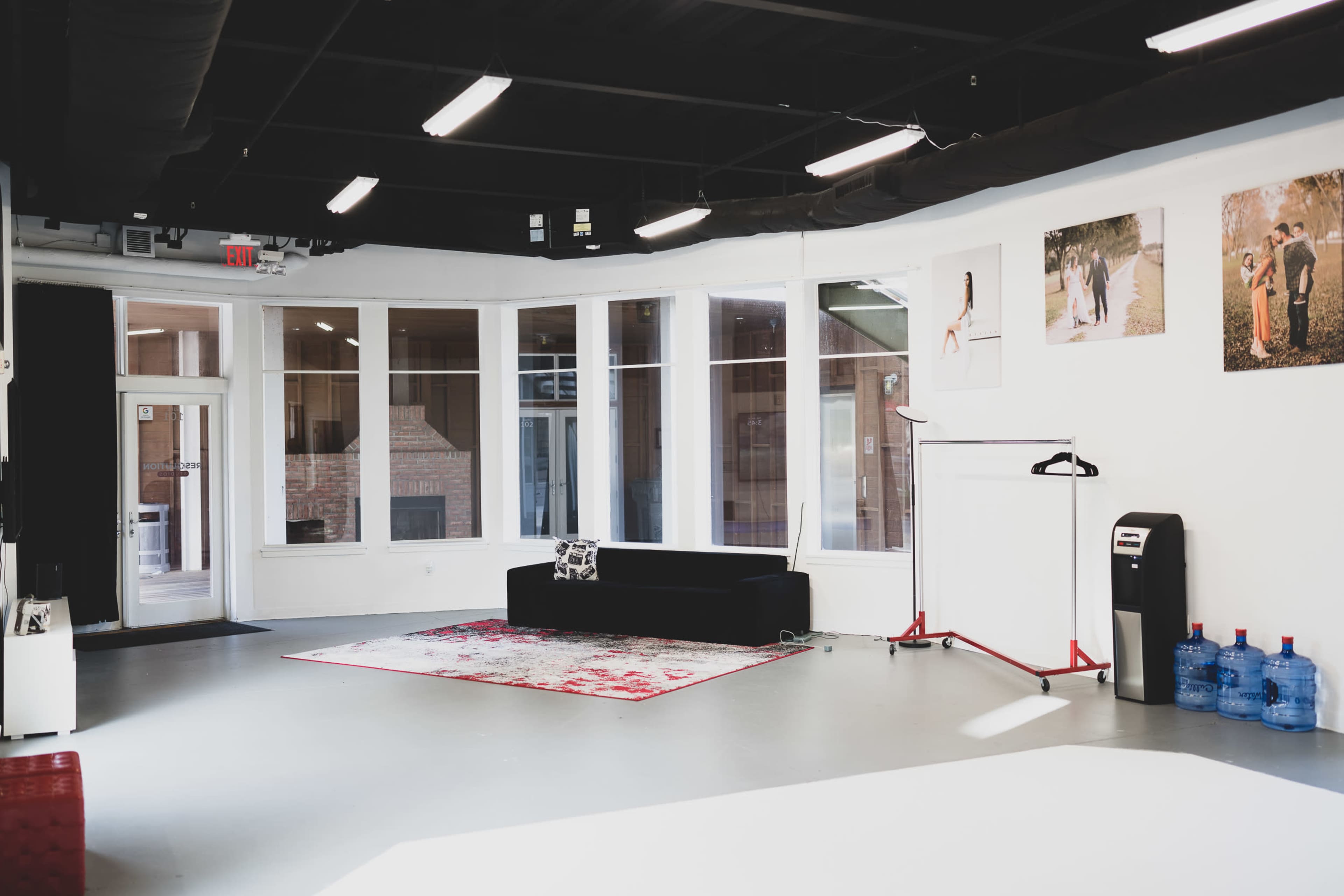 A modern, spacious interior with large windows, a black couch, a patterned rug, and a clothing rack.