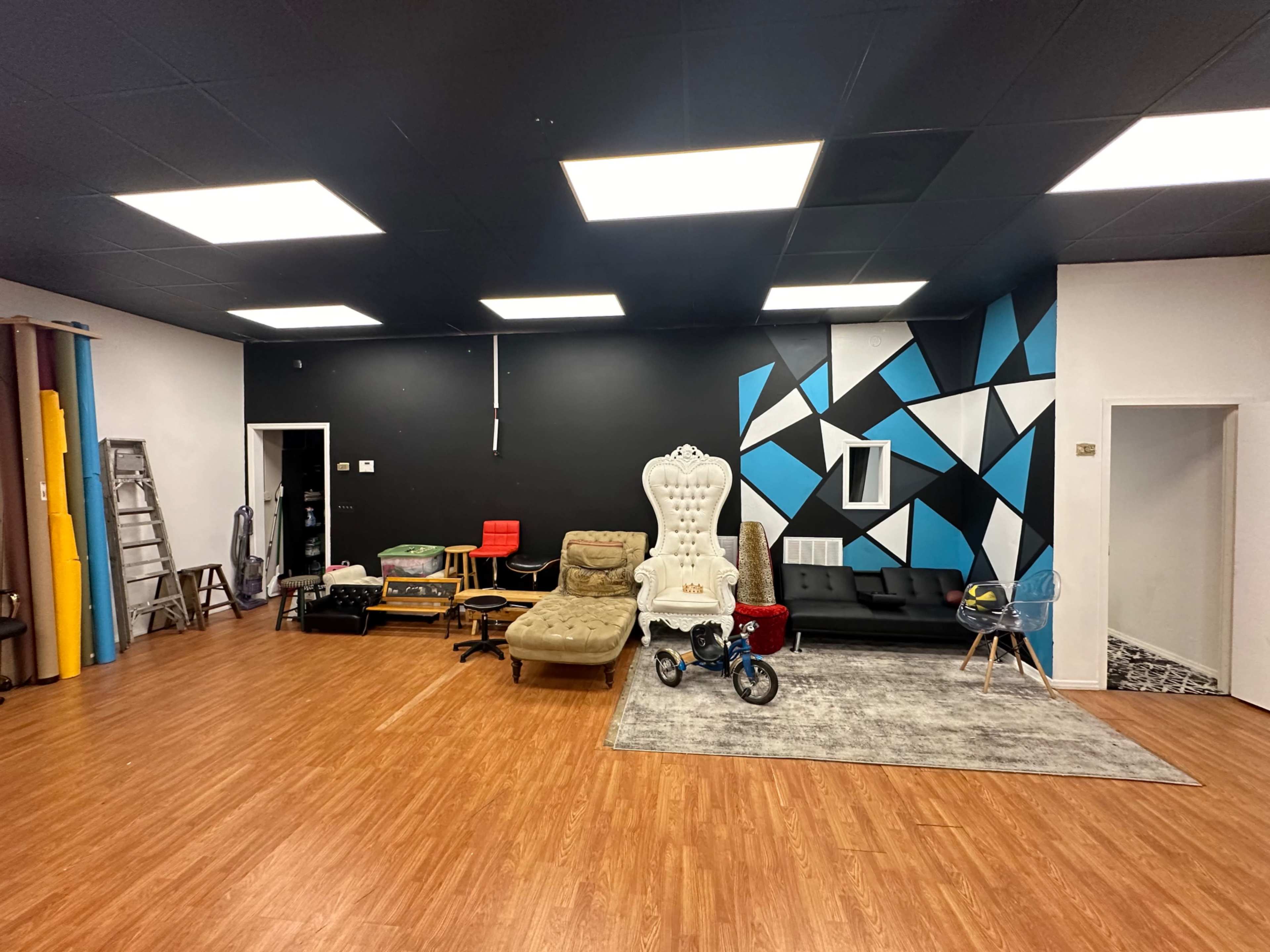 A spacious room with mixed furniture, including a large white chair, a couch, and various colorful backdrops, against a black and blue accent wall.
