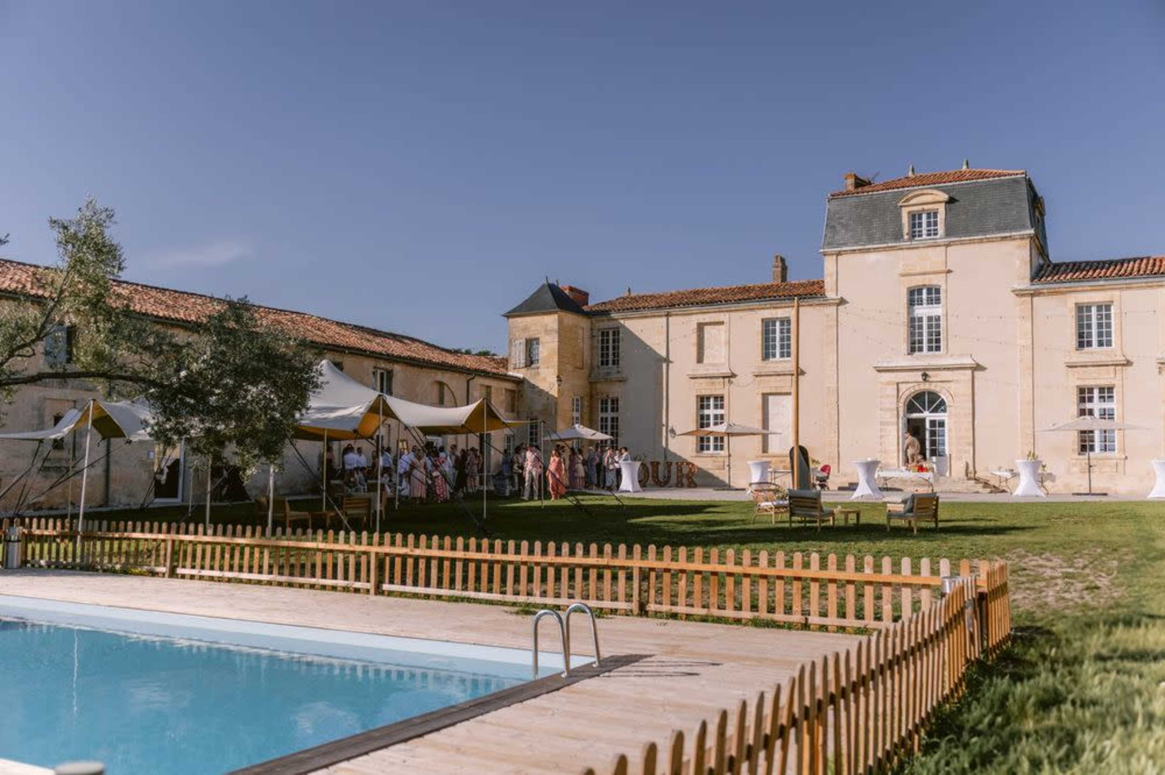 A large estate features a swimming pool and a gathering under a tent in the backyard.